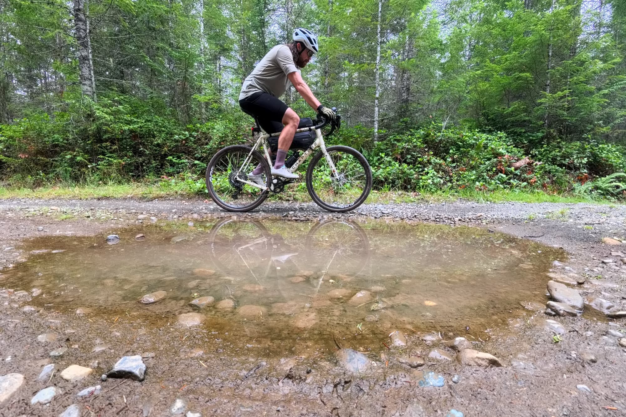 Jeff rides his gravel bike past a large puddle on a forest service road.
