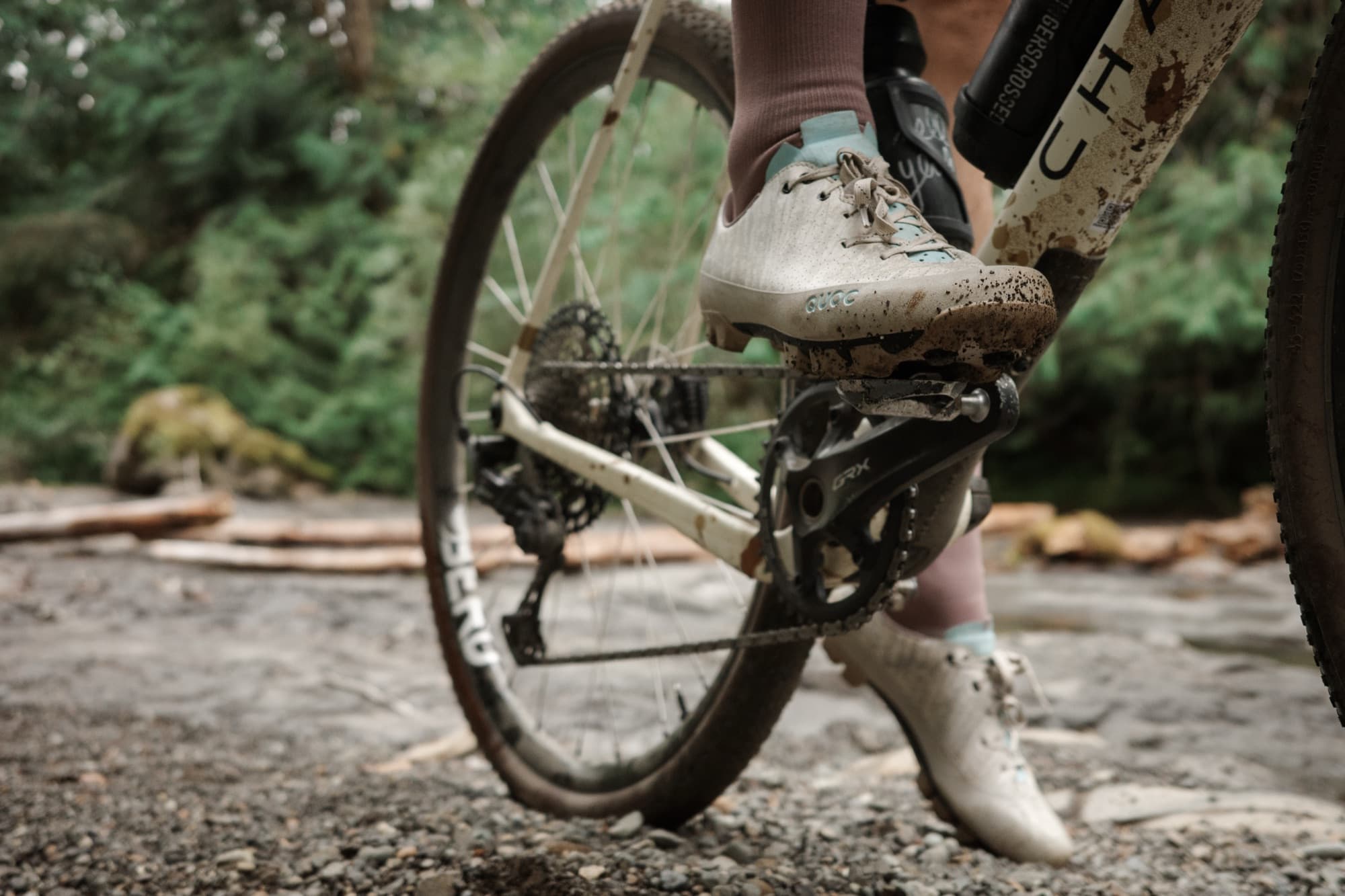 A muddy Gran Tourer XC Lace on the pedal beside a riverbank.