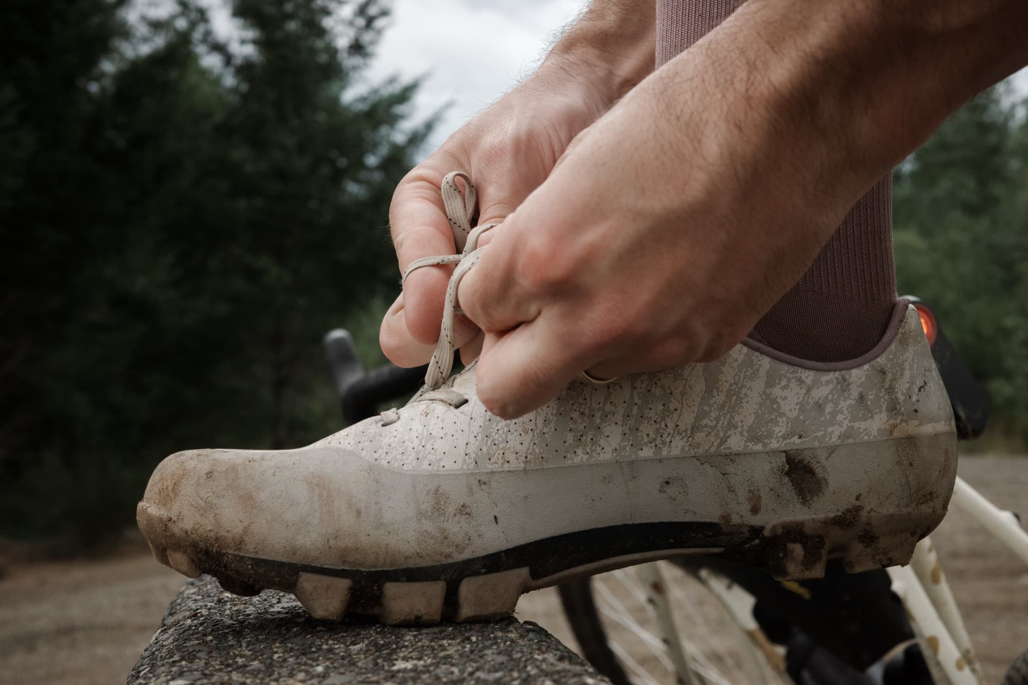 Jeff laces up a muddy Gran Tourer XC Lace, foot propped on a rock beside his bike.