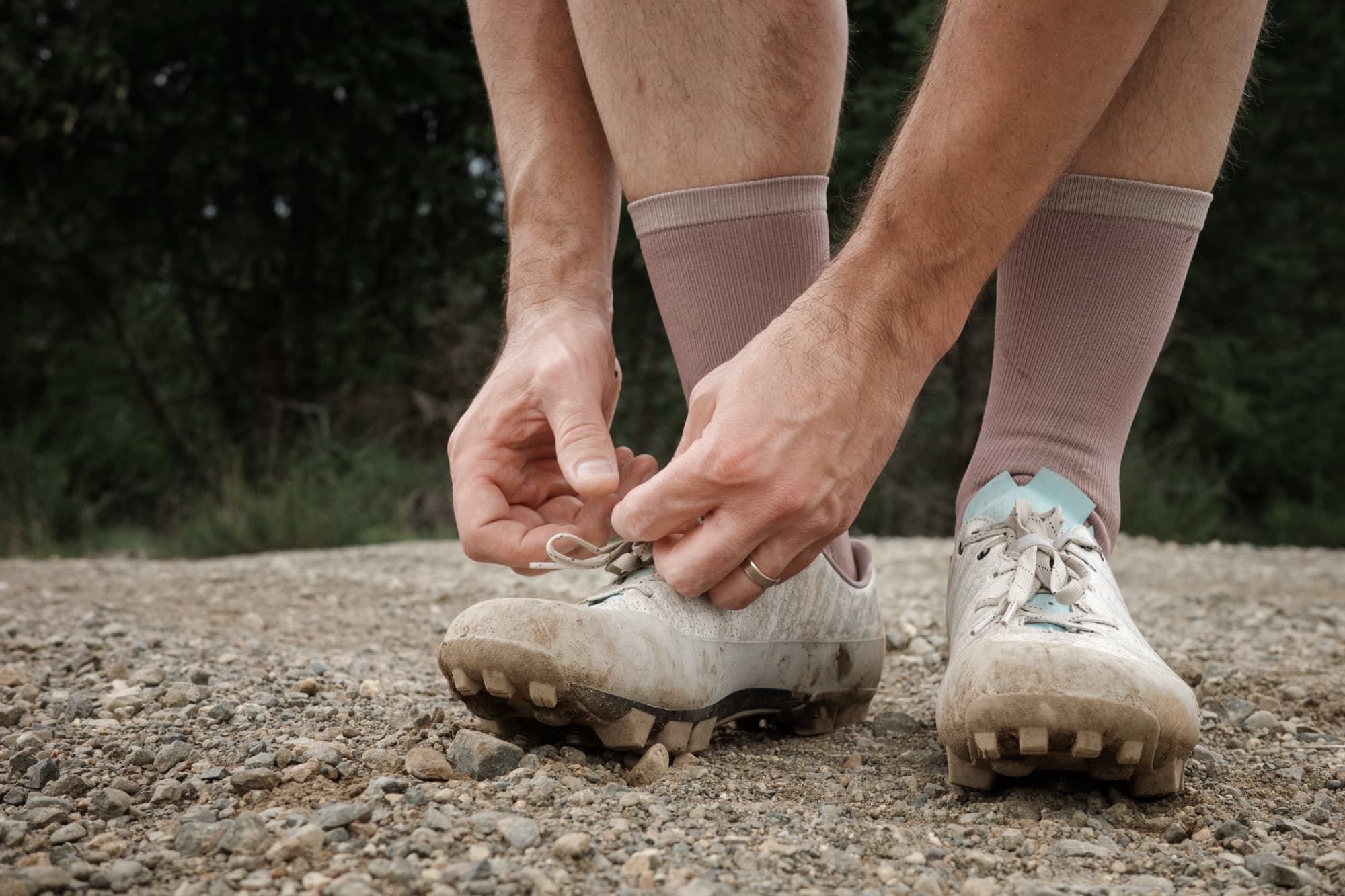 Jeff ties his laces standing on a gravel road.