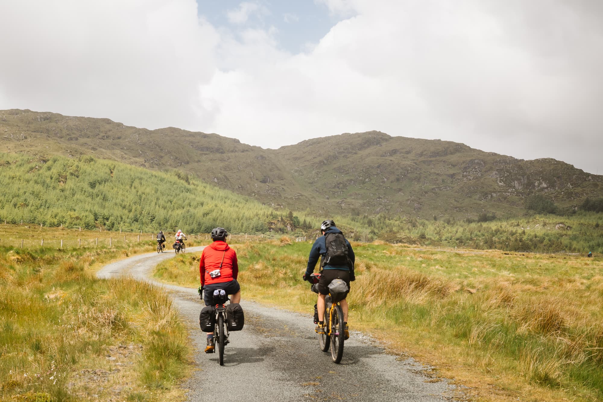 Two loaded riders climb a backroad between green hills