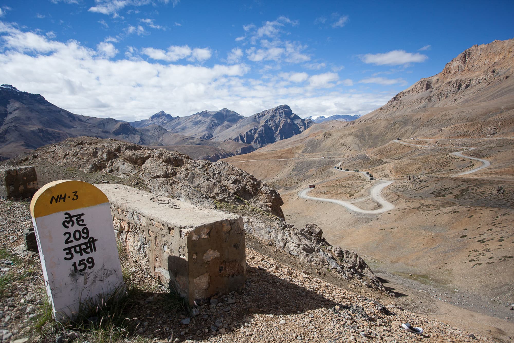 A stone road marker on a high mountain pass with switchbacks below.