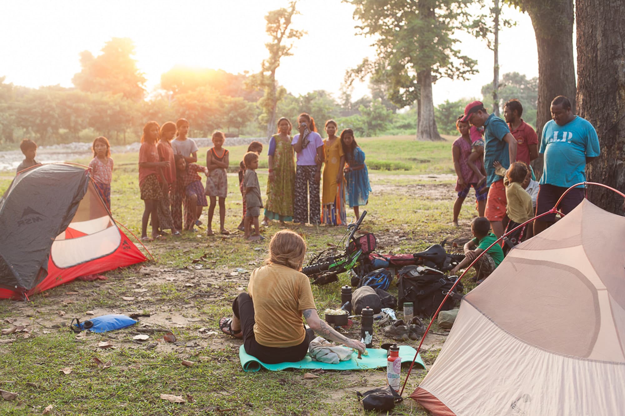 A camp at golden hour as local children gather nearby.
