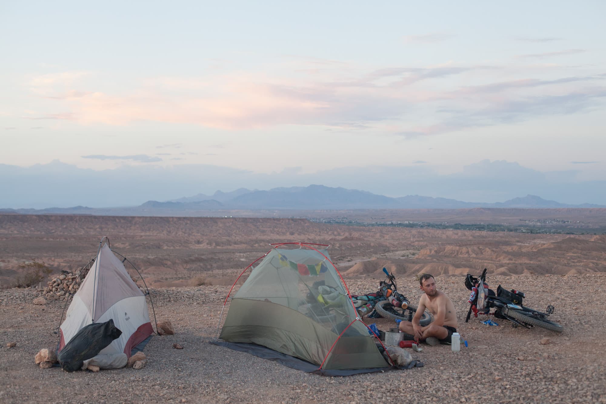 Tents pitched on open desert ground at dusk with mountains in the distance.