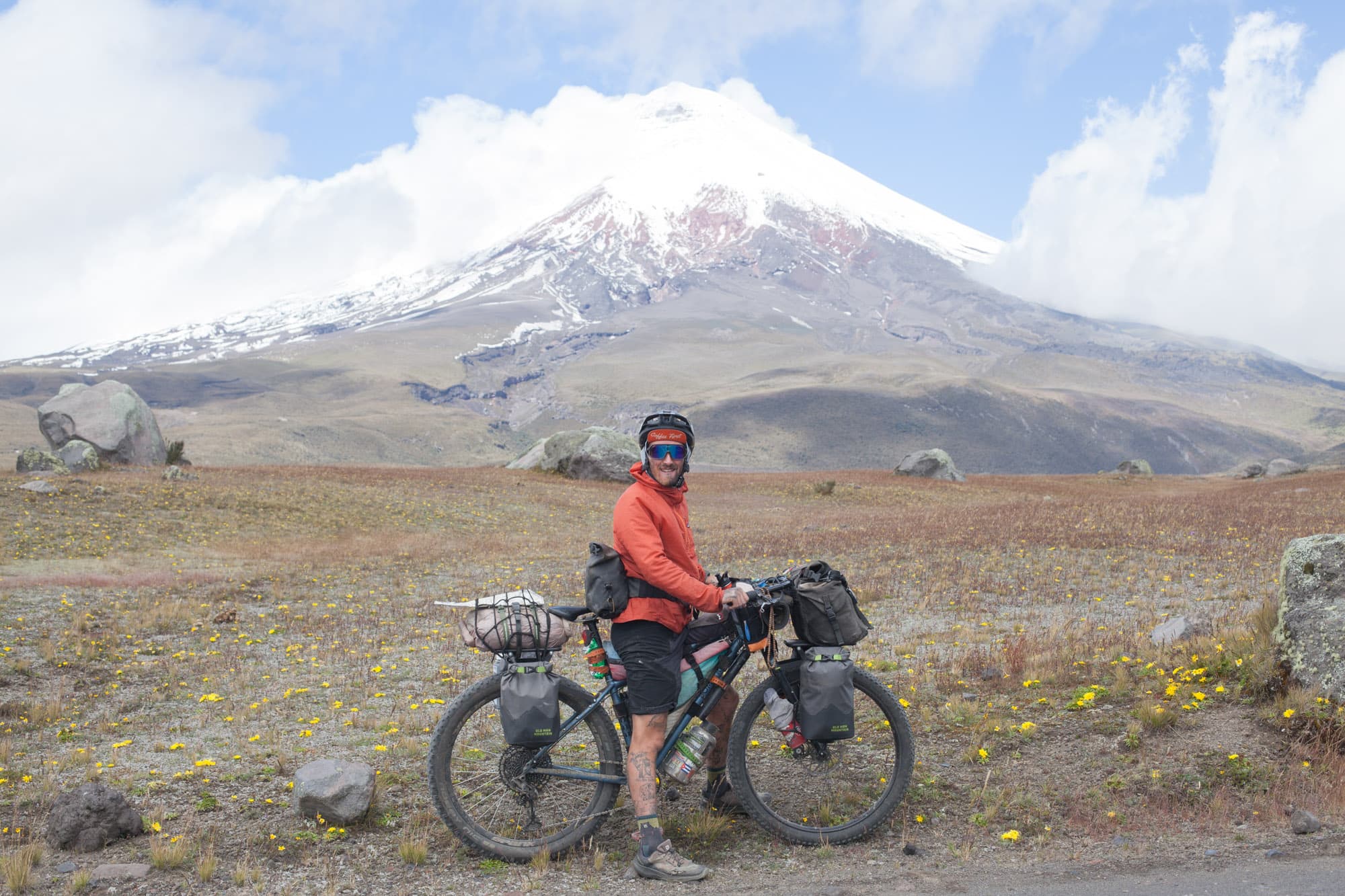 Clotaire stands with his loaded bike below a snow-capped volcano.