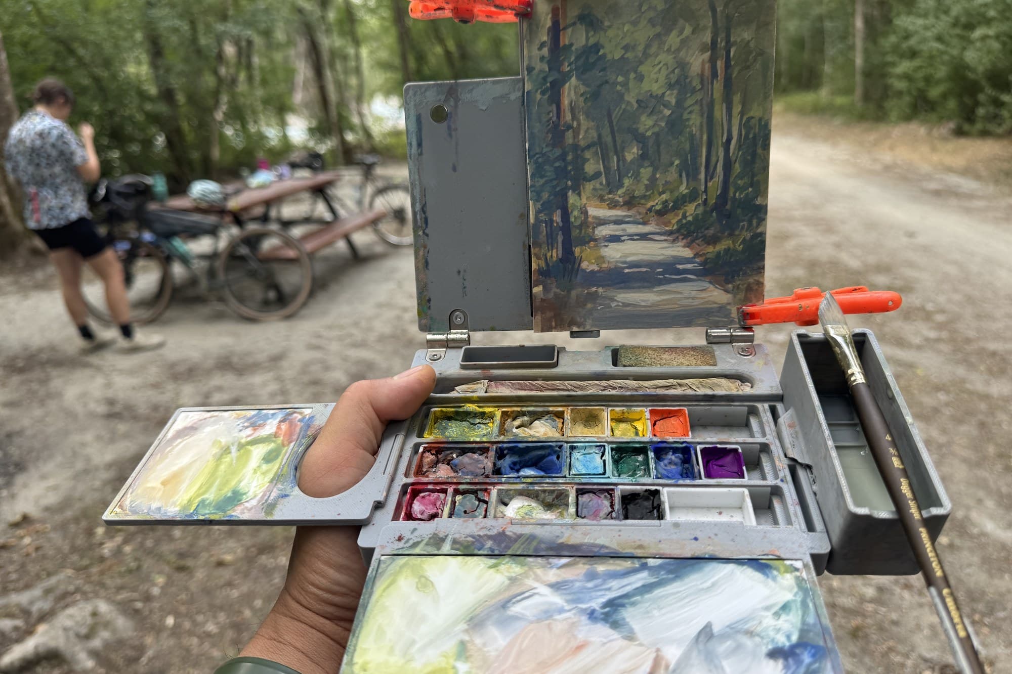 Russ holding his painting kit on a gravel road with bikes behind