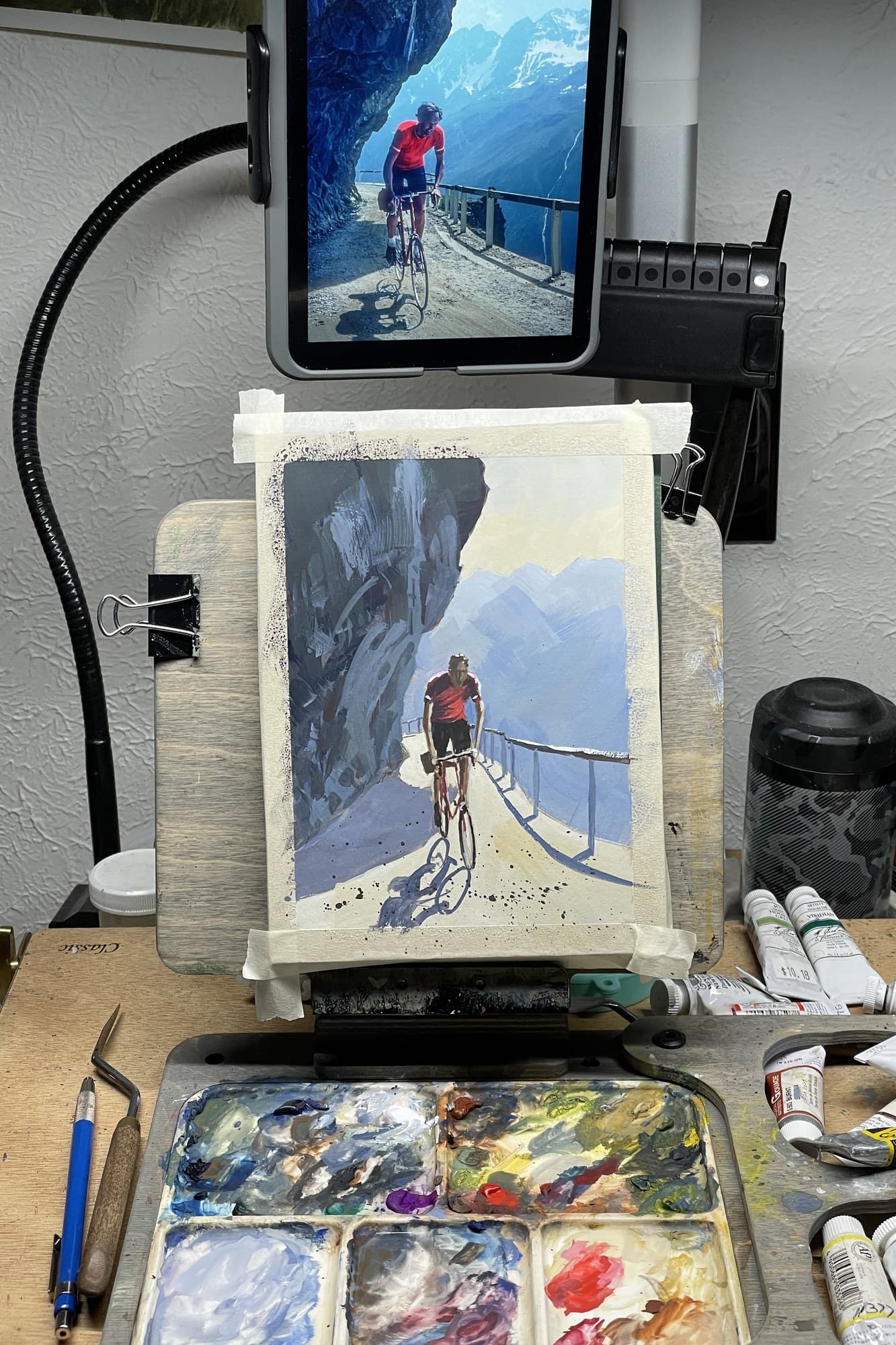 Studio easel with a cyclist painting and a phone reference photo