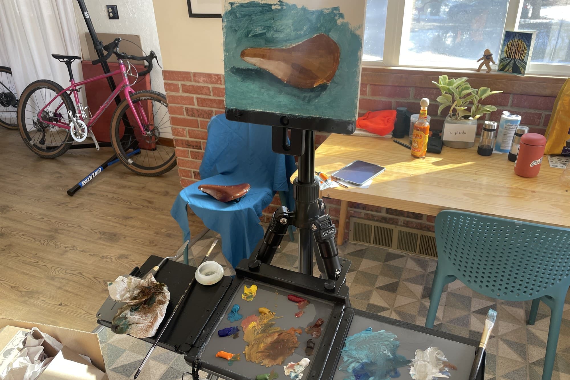 Russ' studio with an easel, a saddle painting in progress, and a pink bike