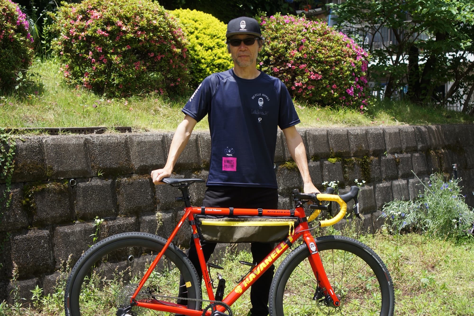 Tetsuro Ohno standing with his red gravel bike against a stone garden wall