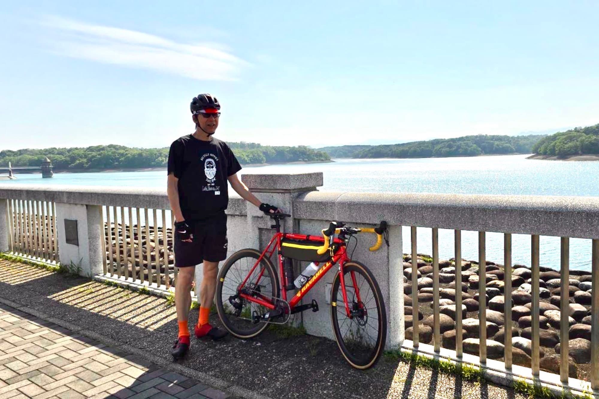 Tetsuro Ohno standing with a red gravel bike on a bridge over a reservoir