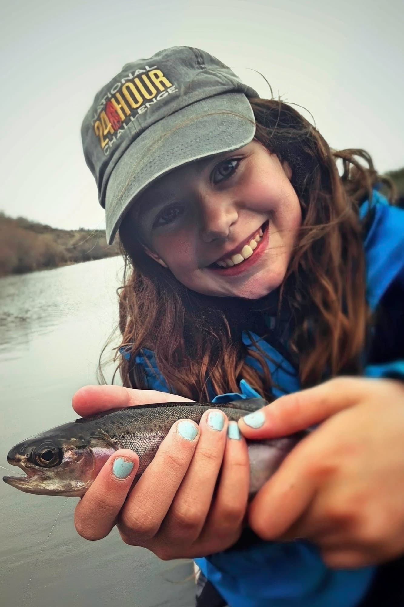 A young girl holding her first rainbow trout beside the water