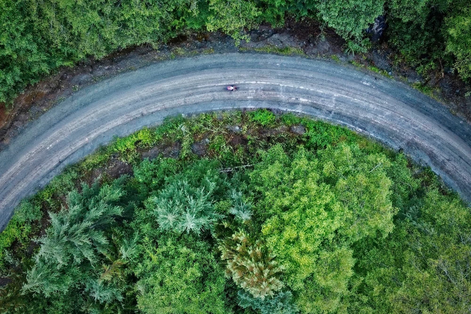 Sweeping bend of gravel from the air, rider mid-corner
