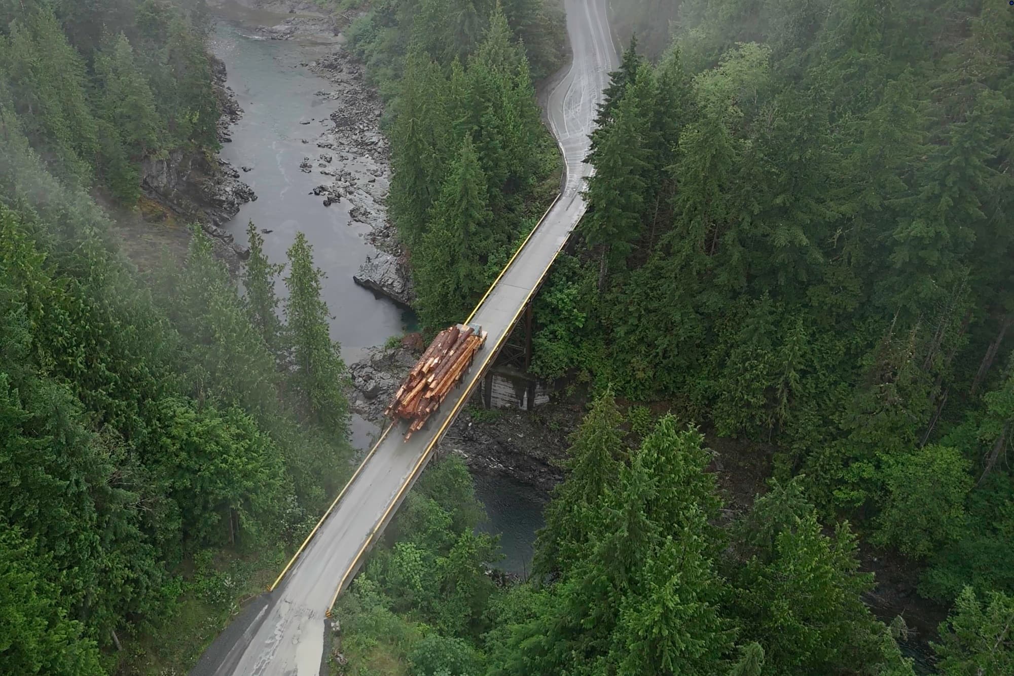 A logging truck crosses a one-lane wooden bridge over the gorge