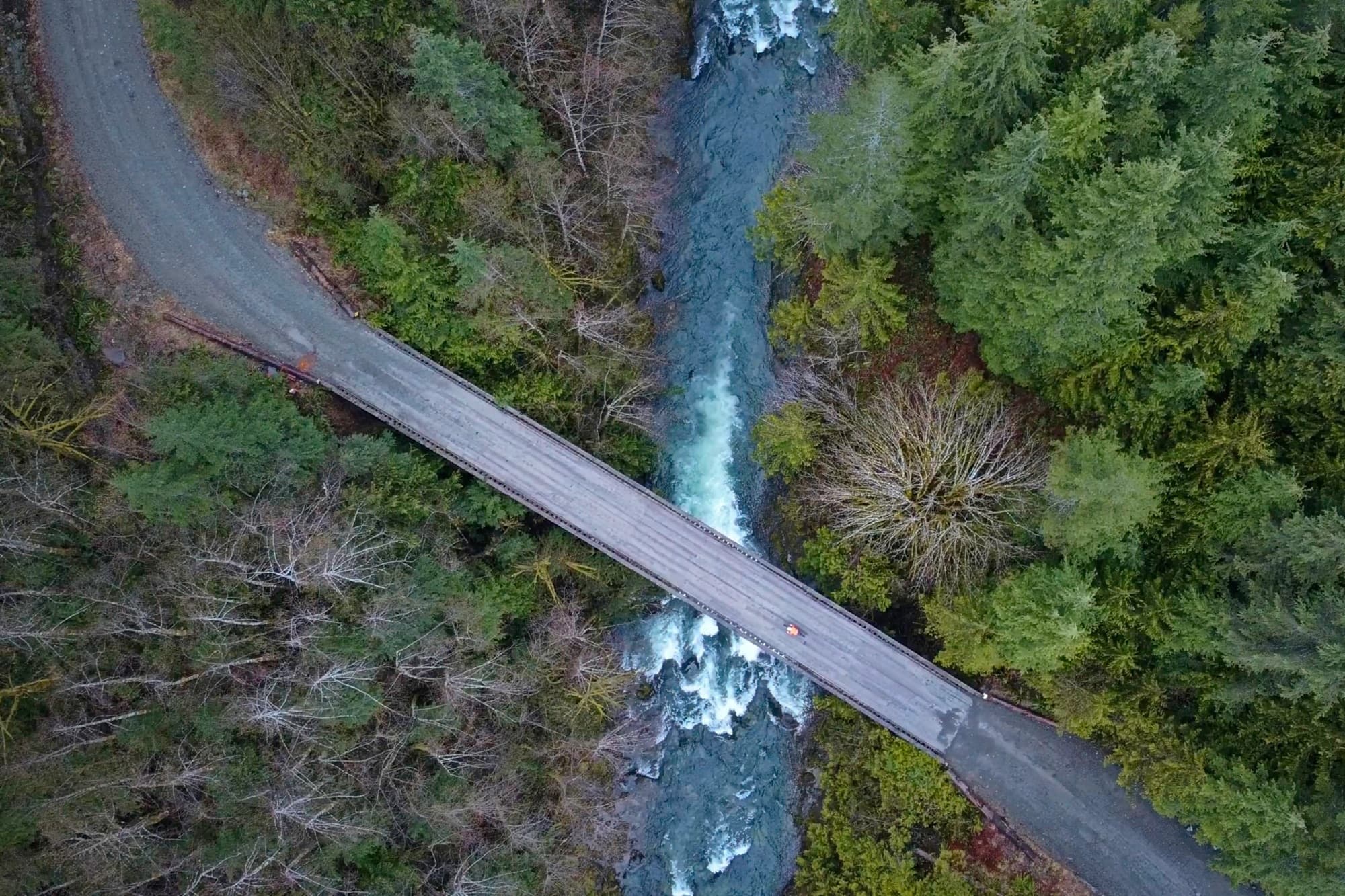 From above, a lone rider crosses a wooden bridge over whitewater