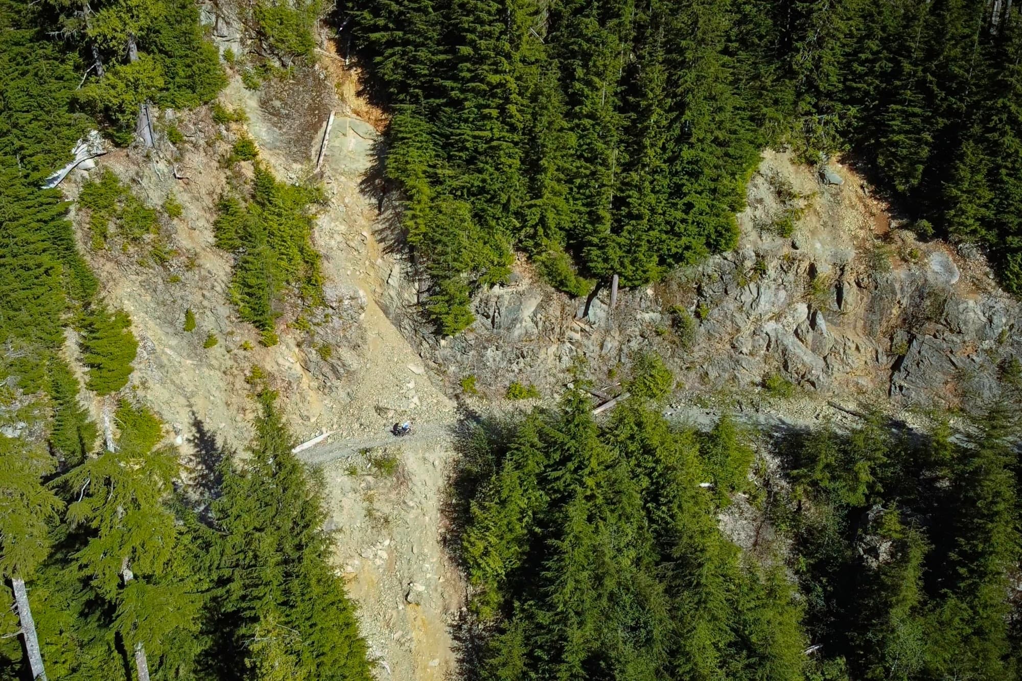 A rider picking through a washed-out section swallowed by slide debris