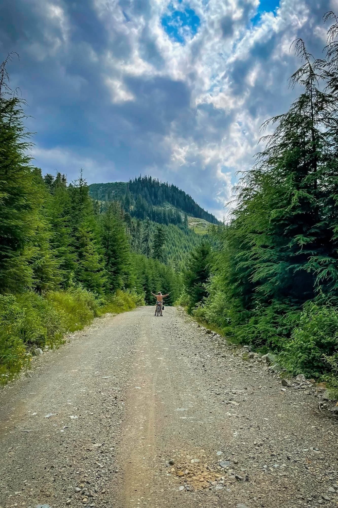 Arms spread wide on a logging road below the peaks