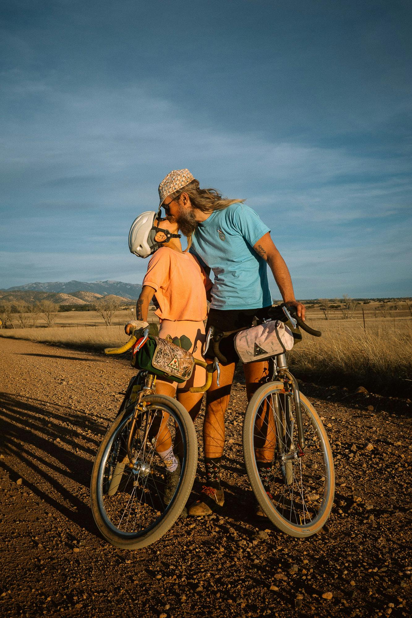 A man and a woman kissing while holding bikes.