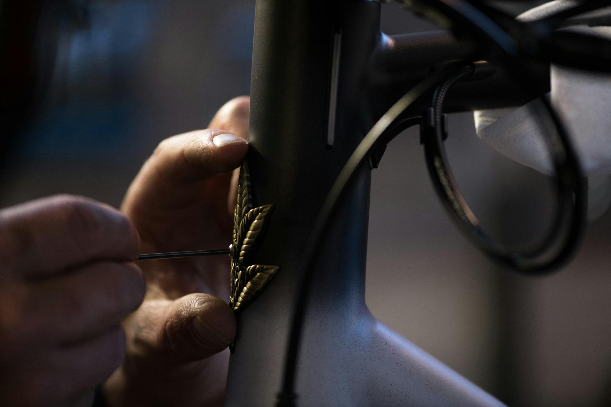 A craftsman adds a head badge to a bike.