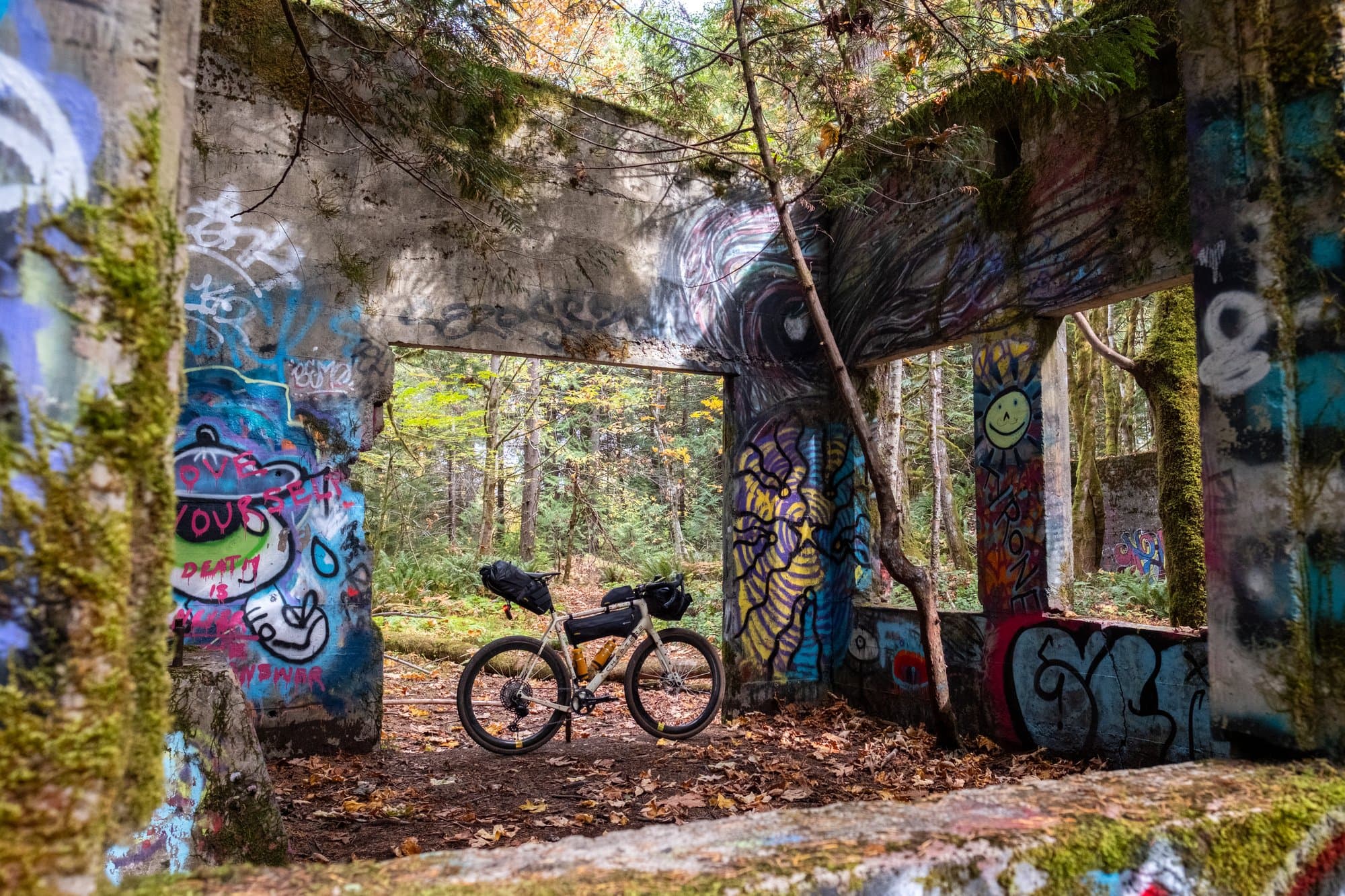 The loaded Kaha standing in an open doorway of moss-covered graffiti ruins in the forest.