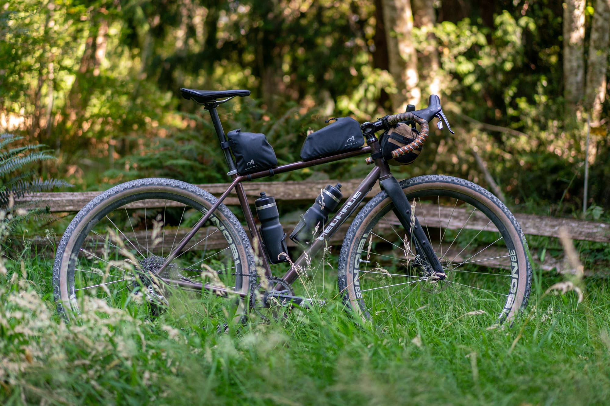 The BigLeaf with both Arkel bags mounted, resting in tall grass by a split-rail fence.