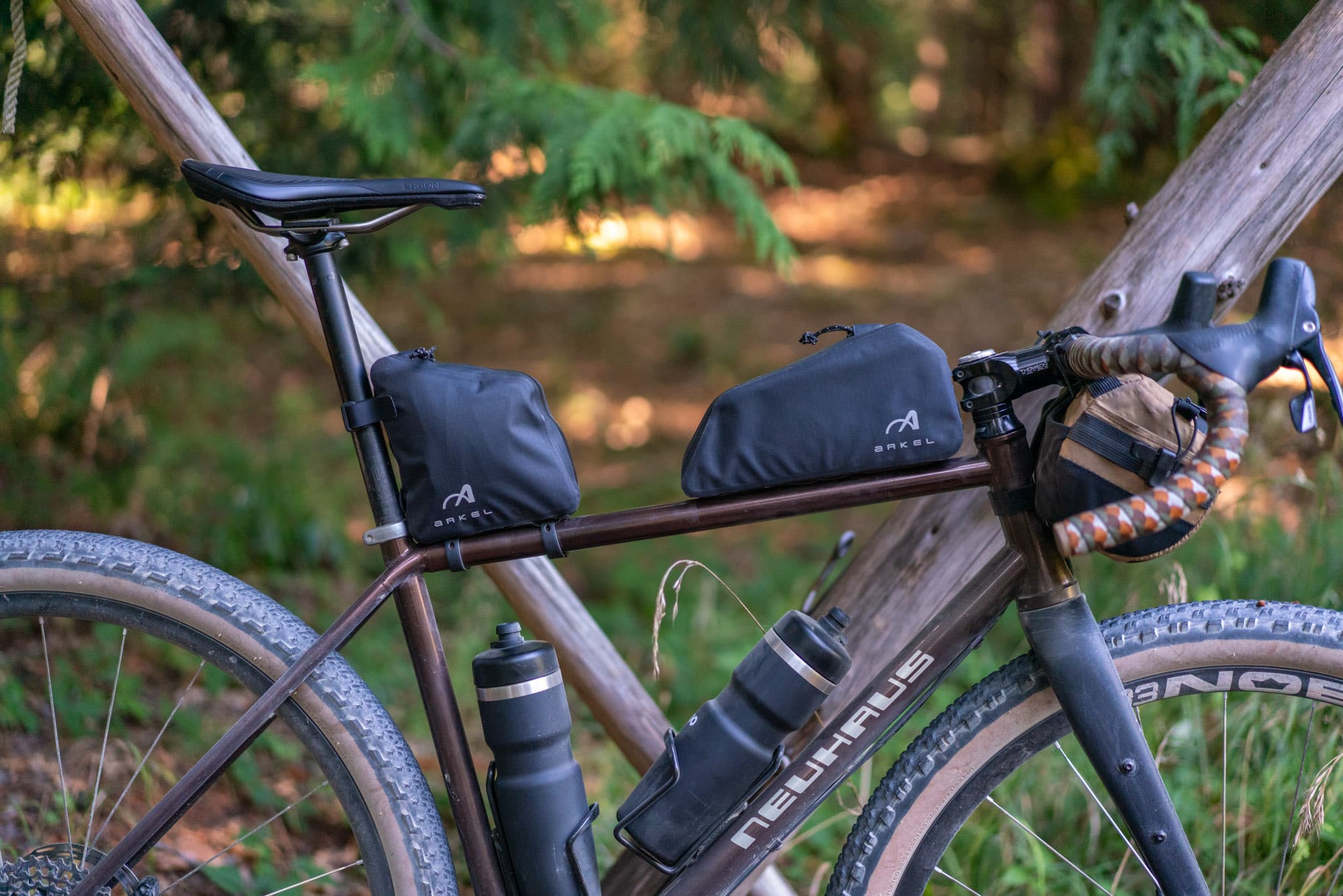 Front and rear Arkel top tube bags mounted against a wood fence backdrop.