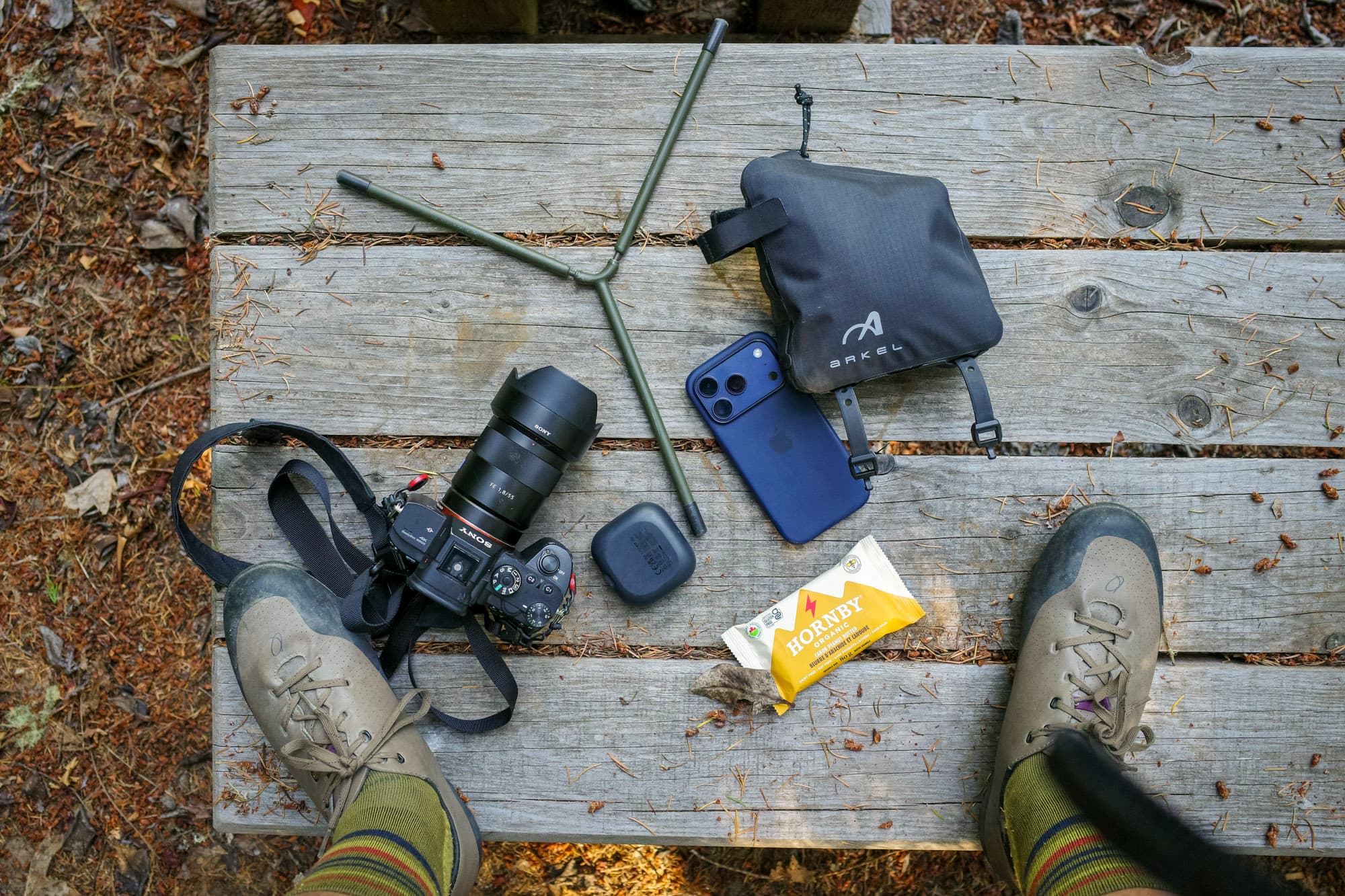 The front bag flat-laid with a camera, phone, earbuds, and a snack bar.
