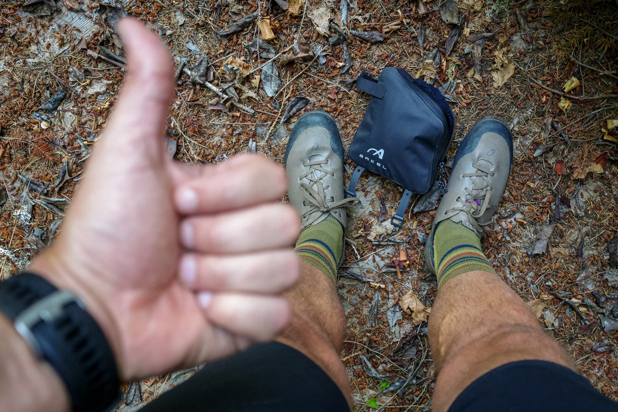 A thumbs up next to the rear bag, set down on the forest floor.