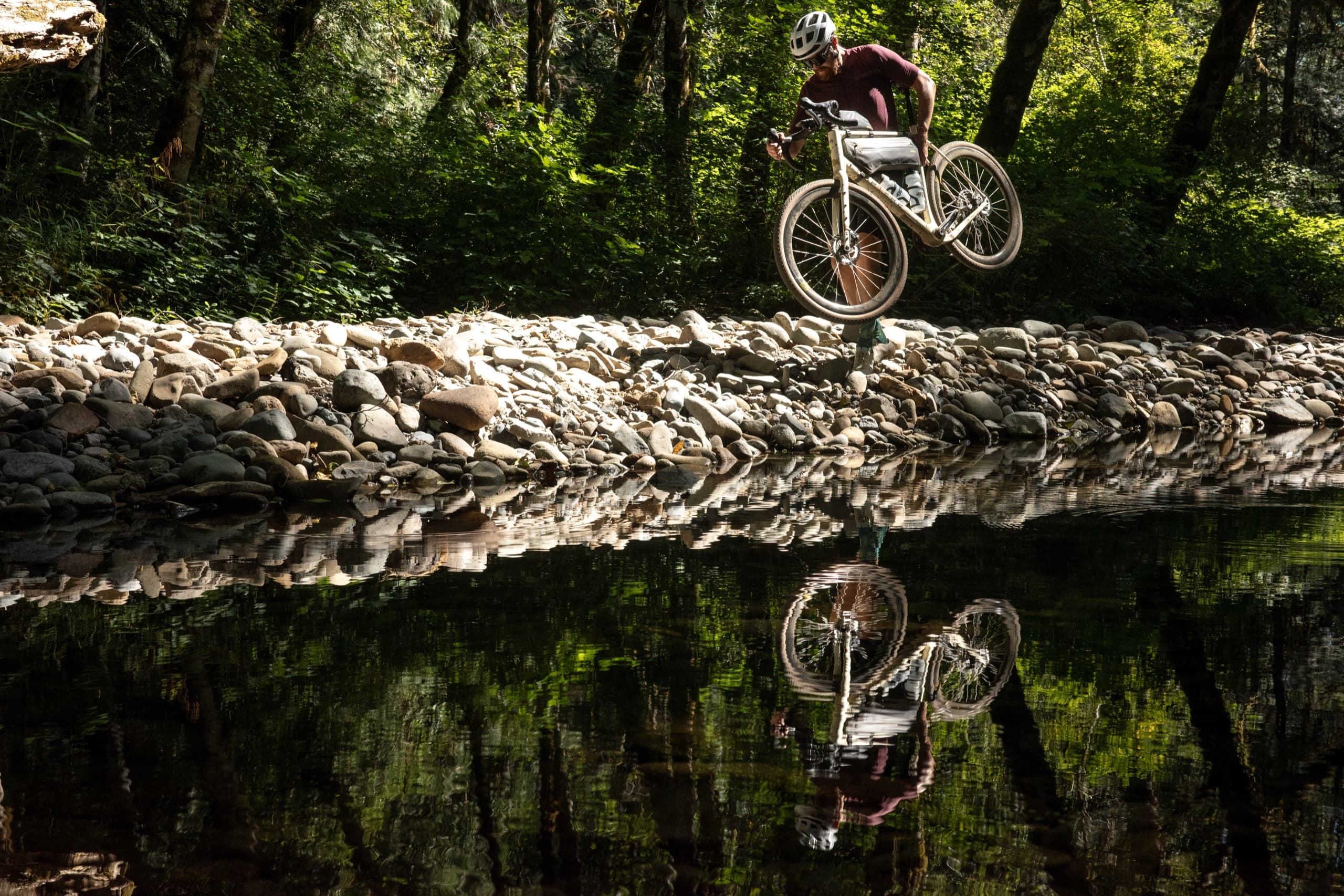 Jeff popping the Kaha over a rocky creek bed, mirrored in the water below.