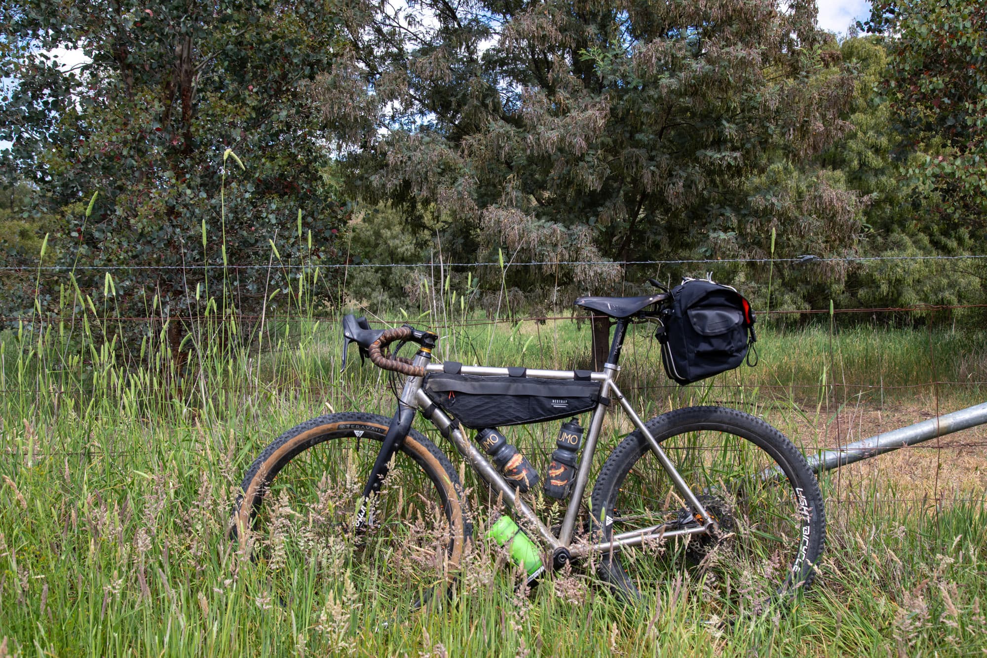The loaded bike resting against a wire fence in tall grass.