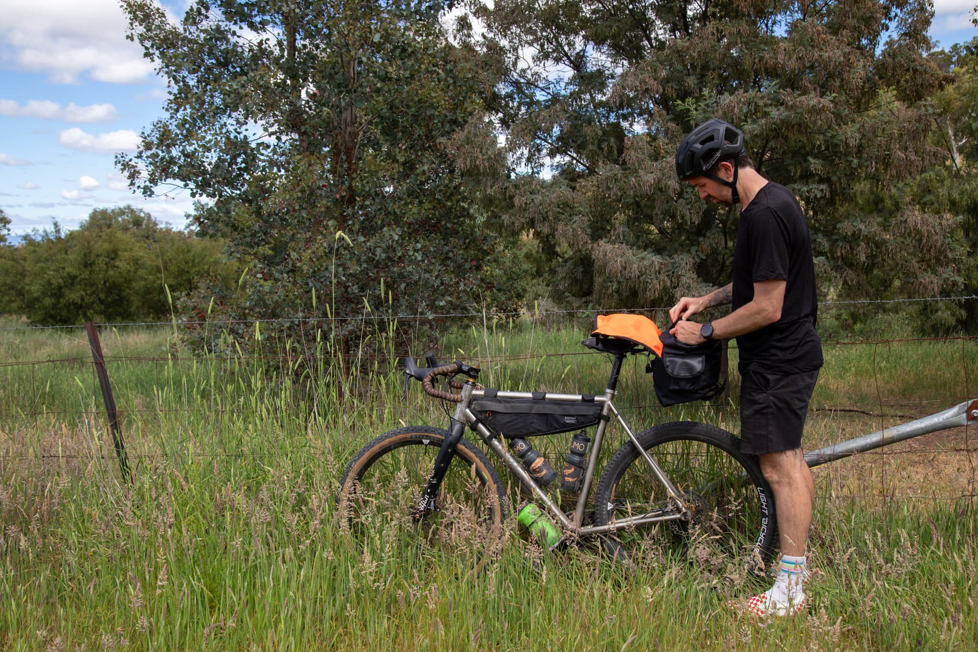 Mattie packing the Carradice Odyssey beside his bike in a grassy field.