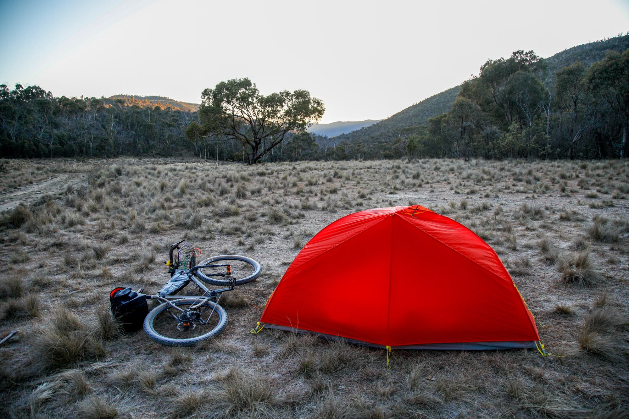 A loaded bikepacking rig beside a tent at a frosty bush campsite.