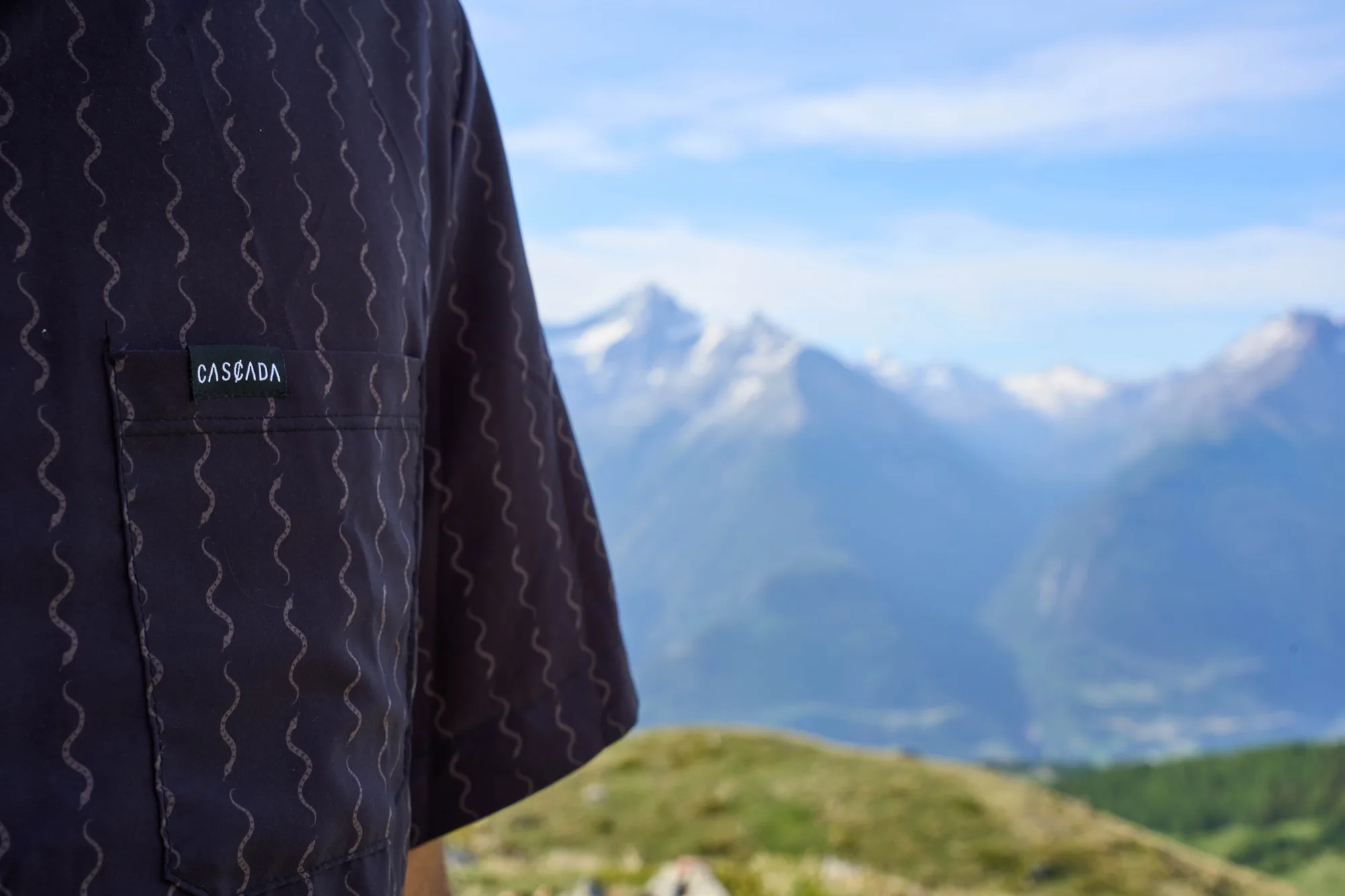 Close-up of the Cascada shirt chest pocket and woven logo label with mountains behind