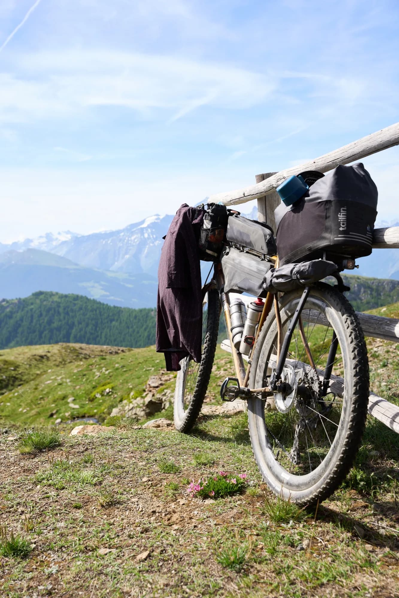 The loaded bike leaning on a fence with the Cascada shirt hung to dry, green Alpine valley behind
