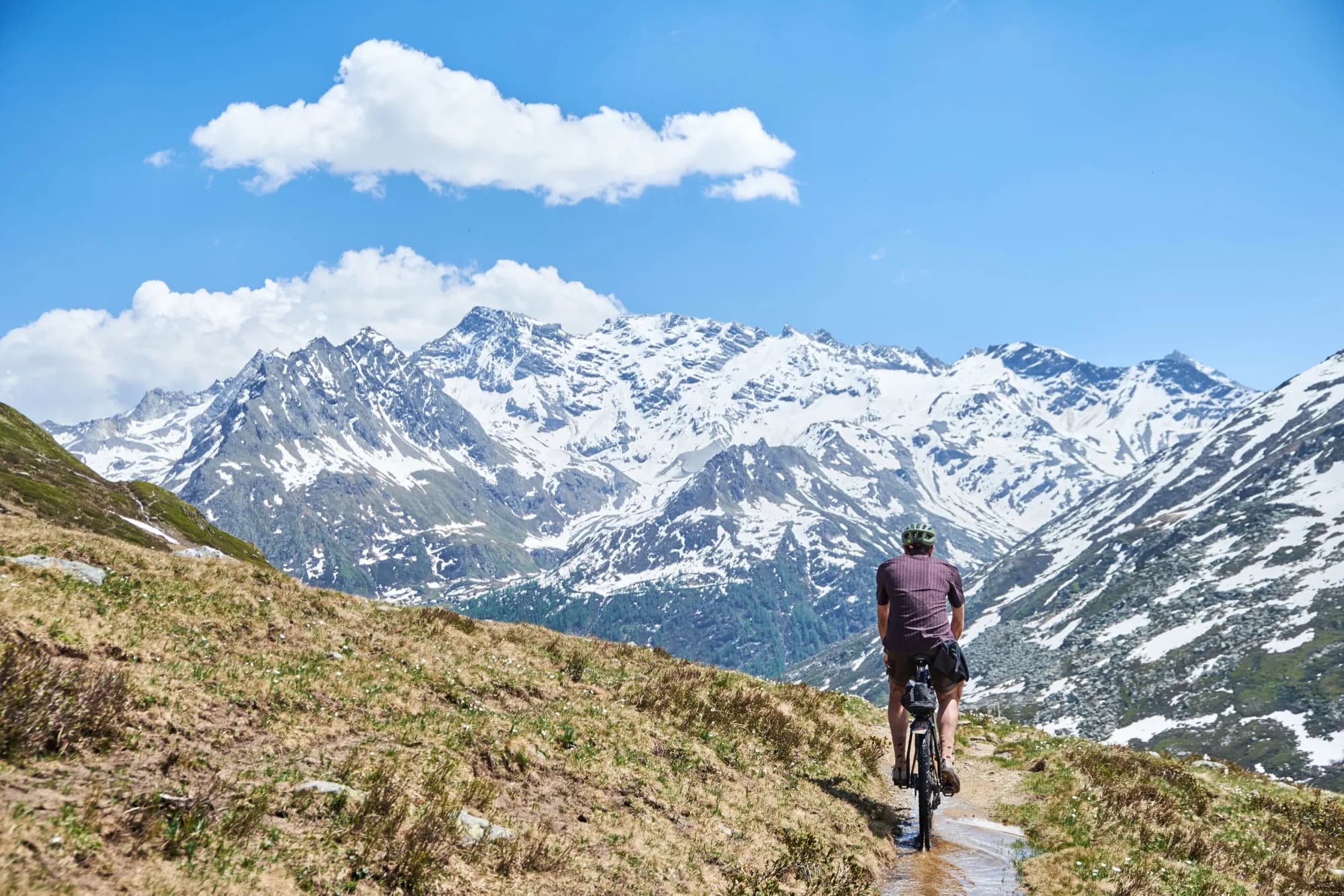 Davide riding down singletrack toward a huge snow-capped Alpine massif in the Cascada kit