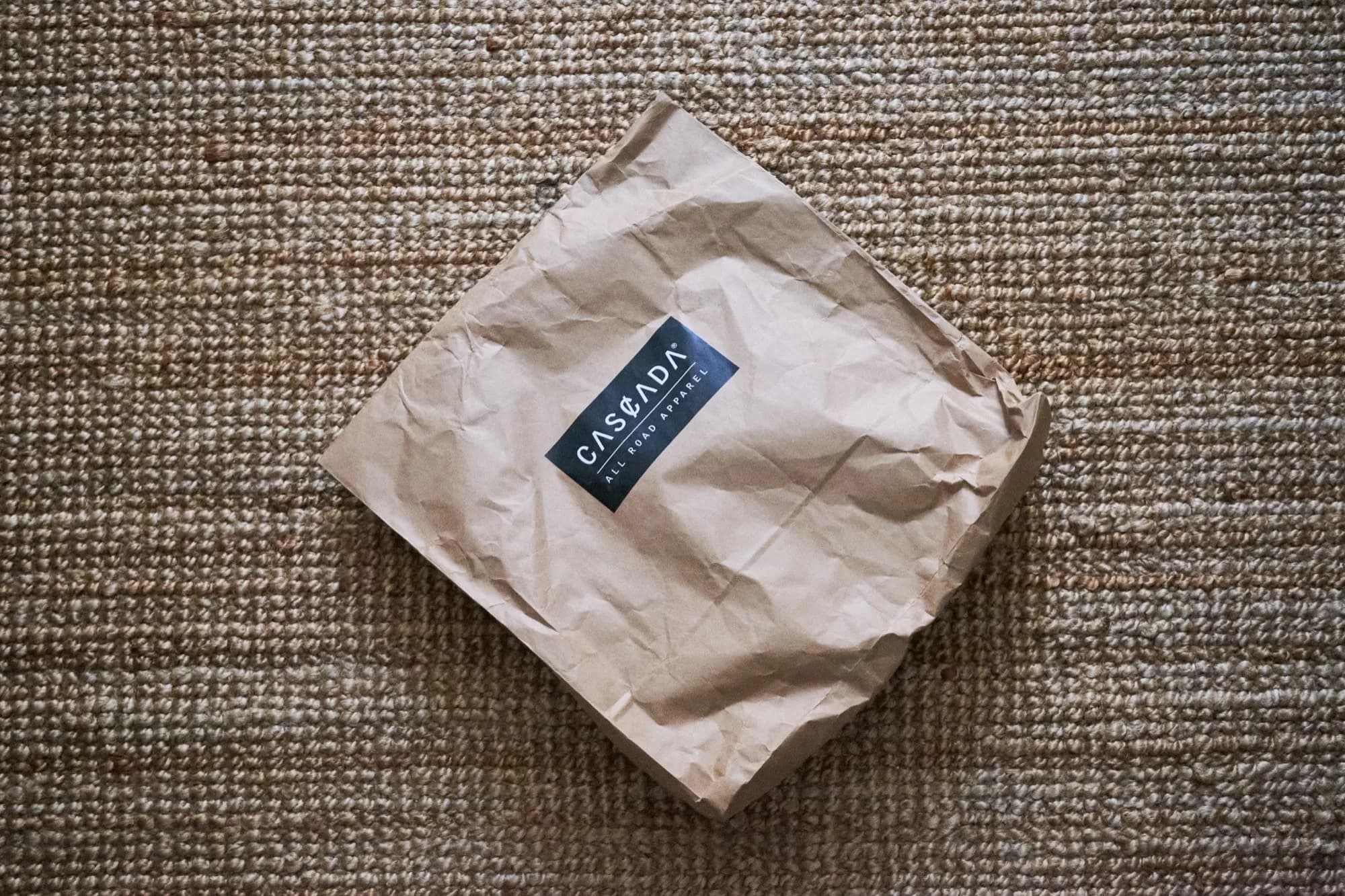The Cascada All Road Apparel kraft-paper package on a woven rug