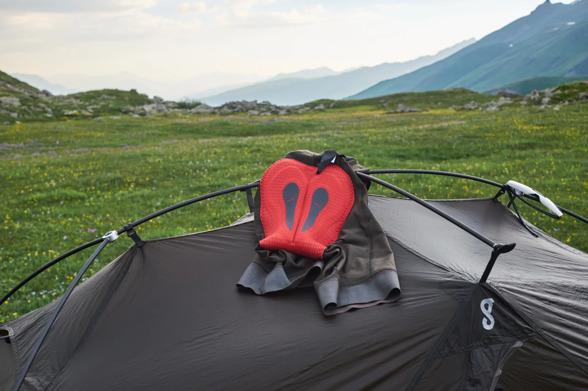 The cargo bib shorts laid over a tent showing the red chamois pad, meadow and mountains behind