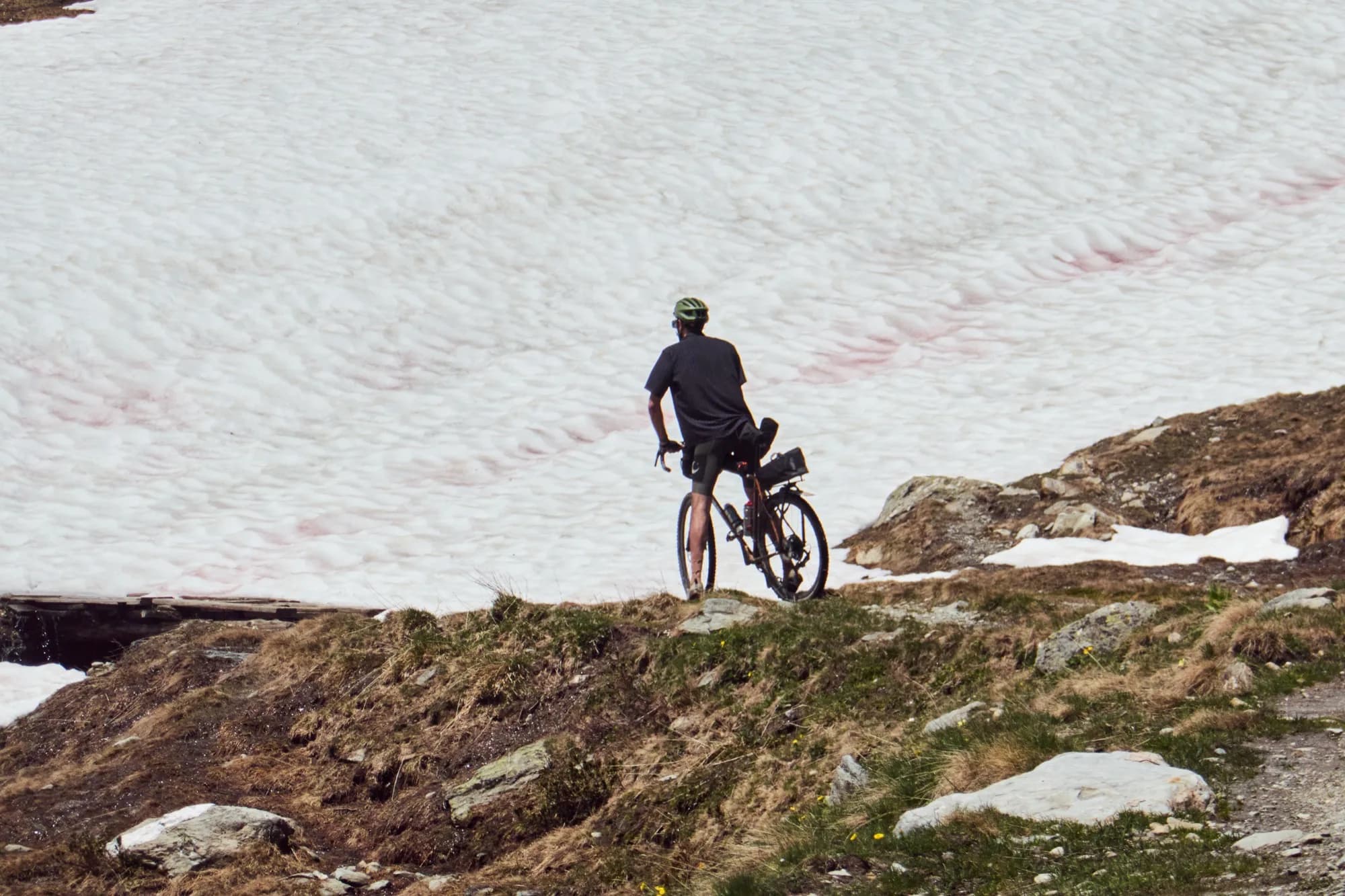 Distant view of Davide walking his bike beside a large snowfield
