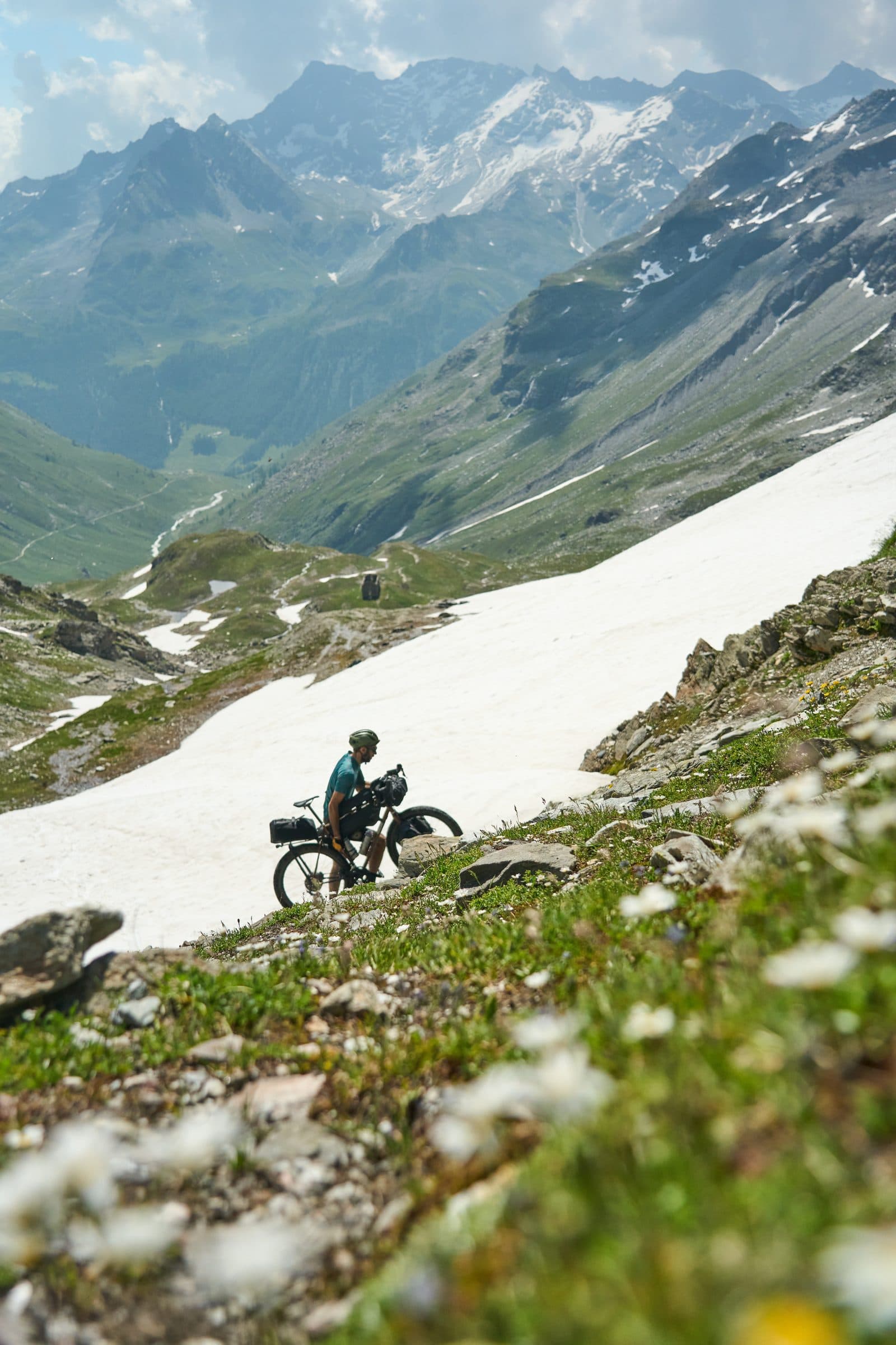 Davide pushing his loaded bike across a melting snowbank in the Alps.