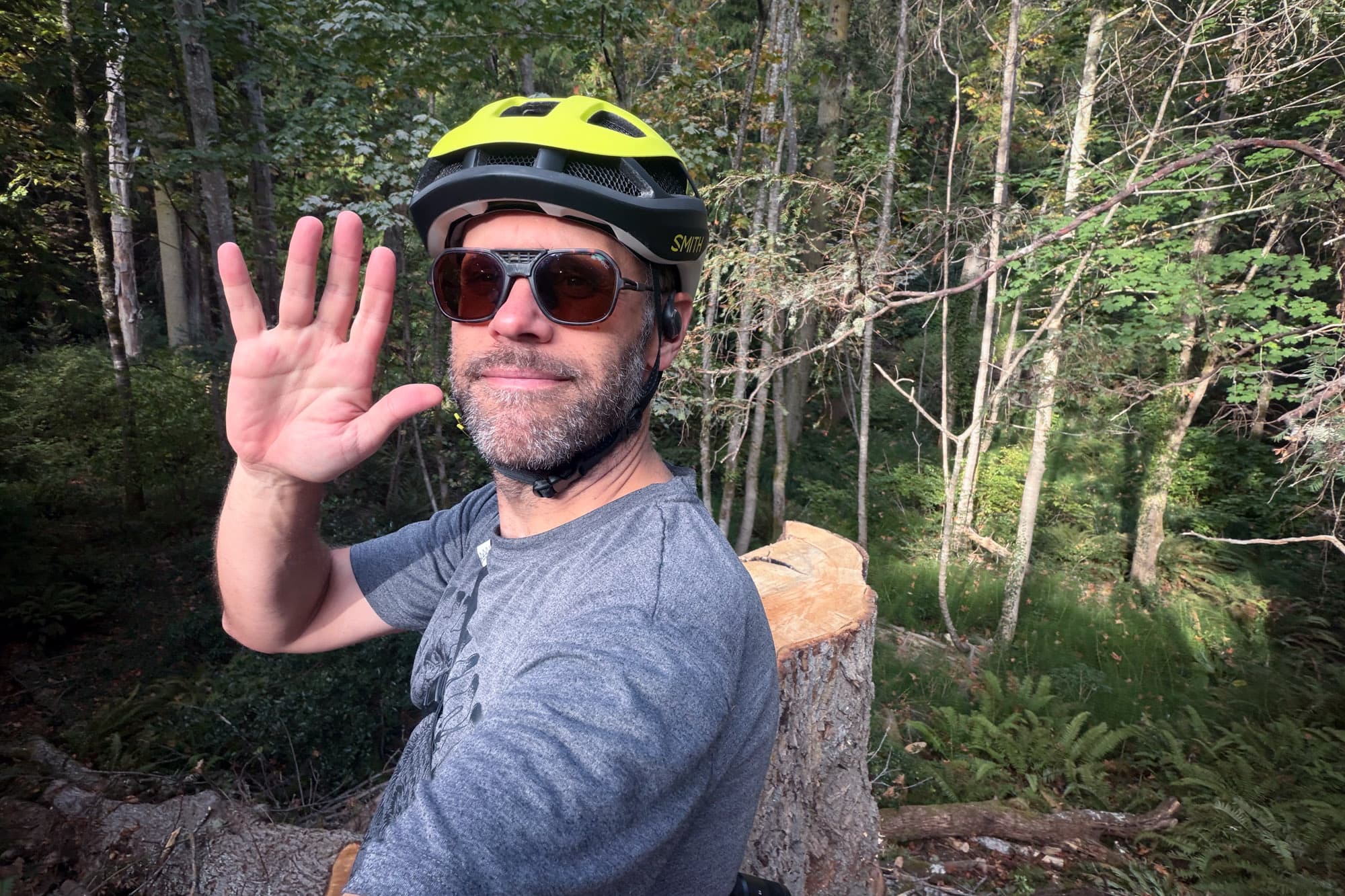 Barry waves goodbye in the Smith Trace, standing beside a stump in the forest.