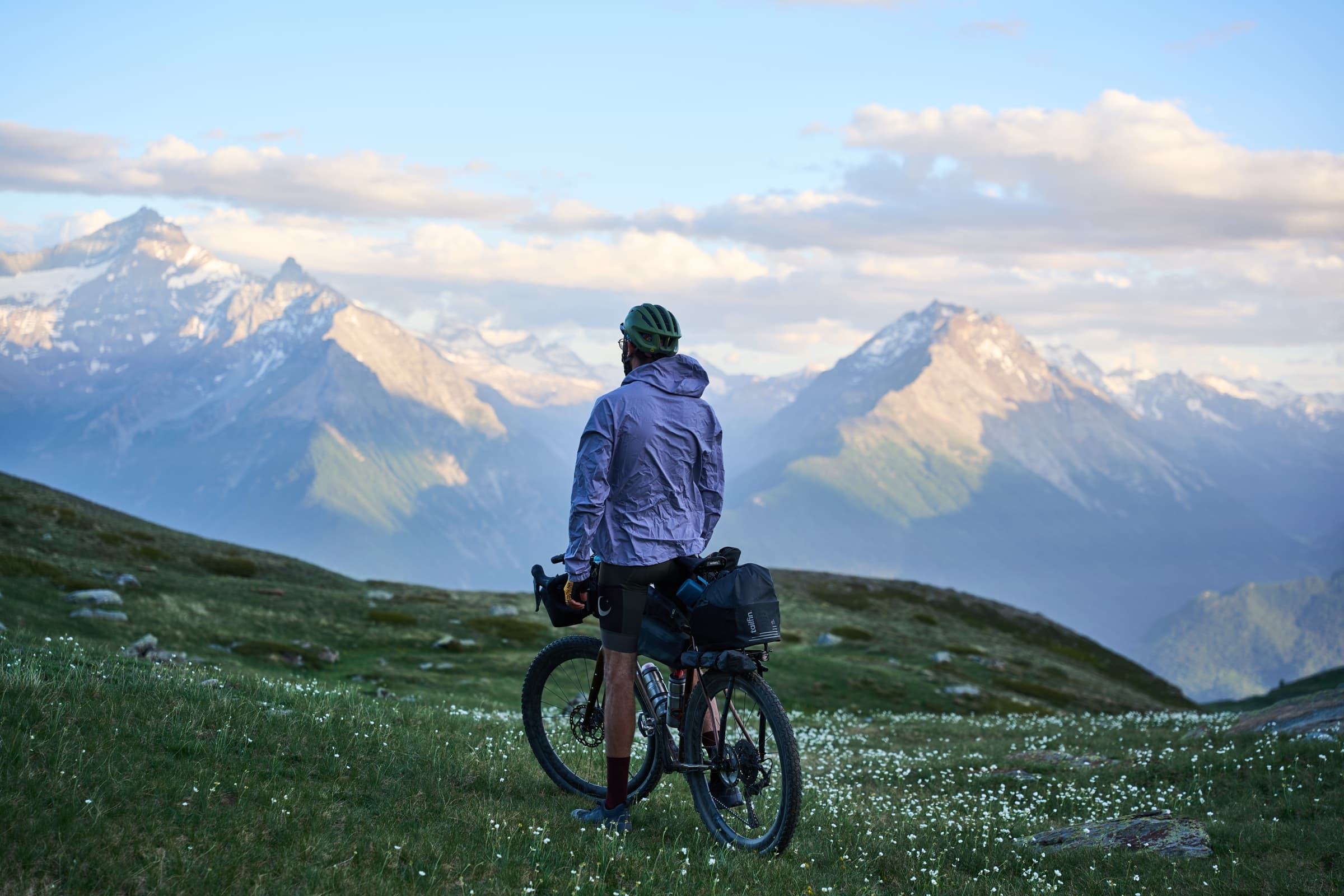 Davide standing beside his loaded gravel bike at an alpine overlook, mountains in the distance.
