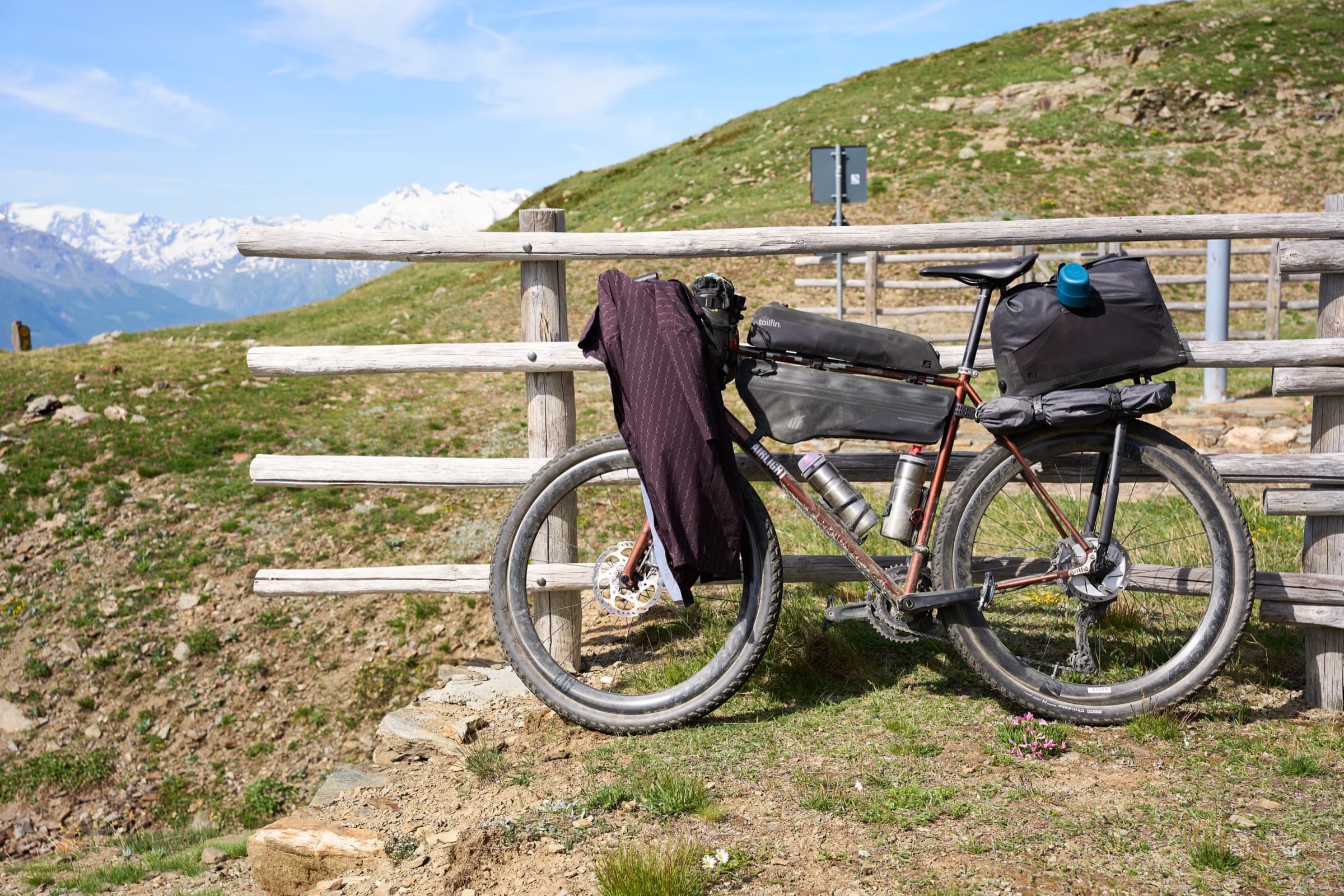 The Tailfin-equipped gravel bike leaned against a wooden fence in an alpine meadow.