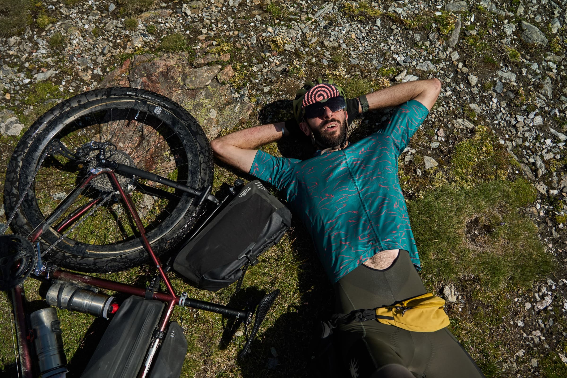 Davide lying on a rocky alpine trail beside his loaded bike during a mid-ride break.