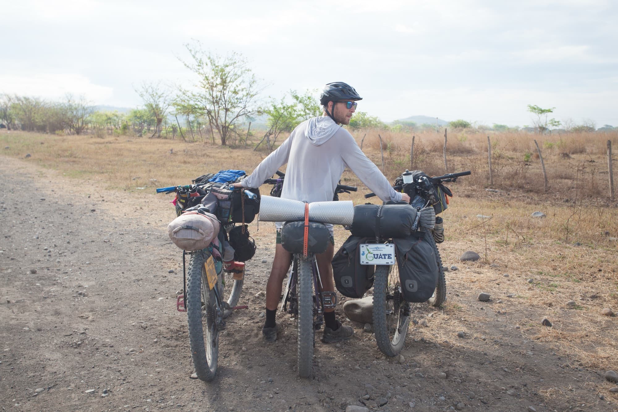 Pushing two loaded bikes up a dry tropical road