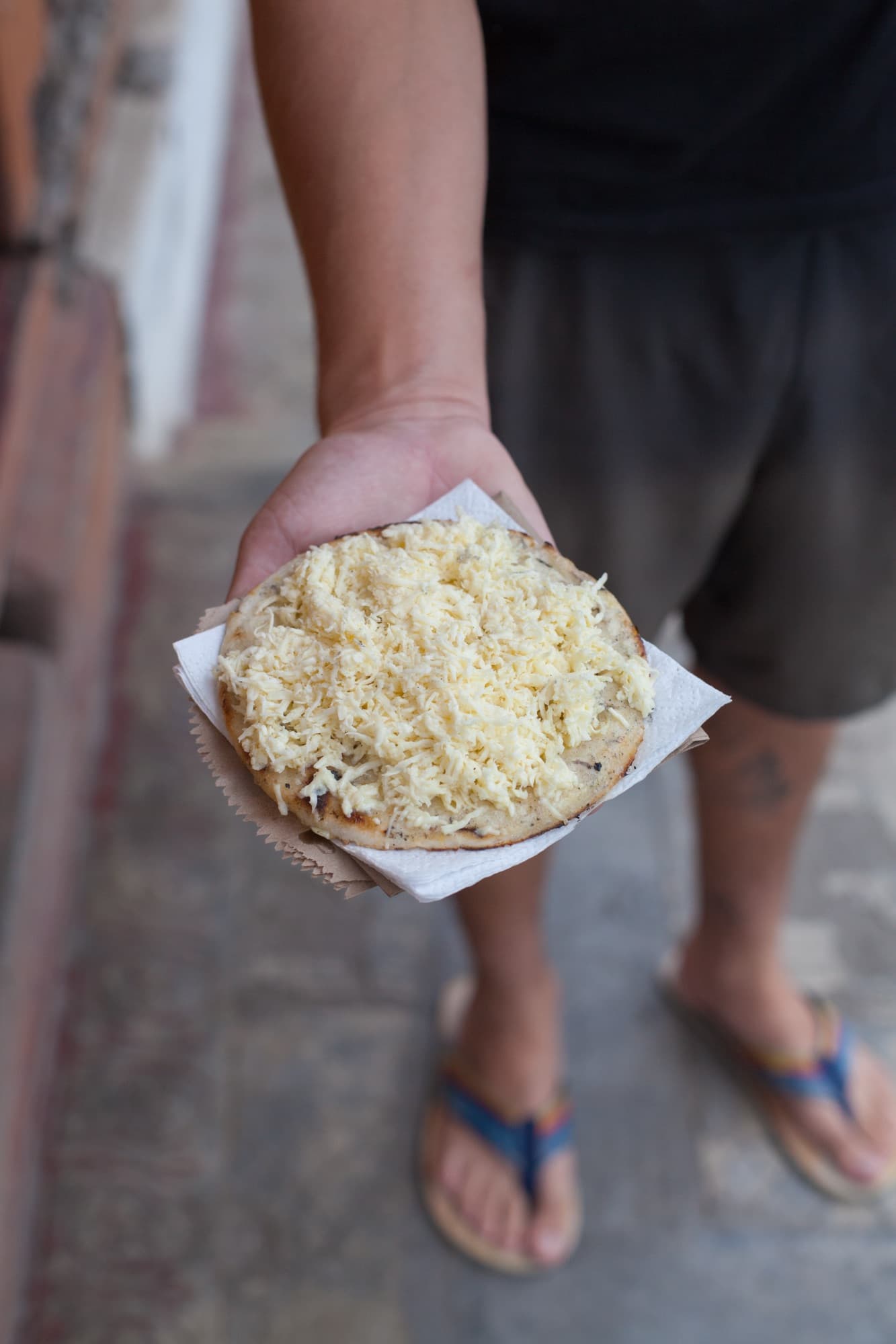 A cheese-topped arepa offered from one hand