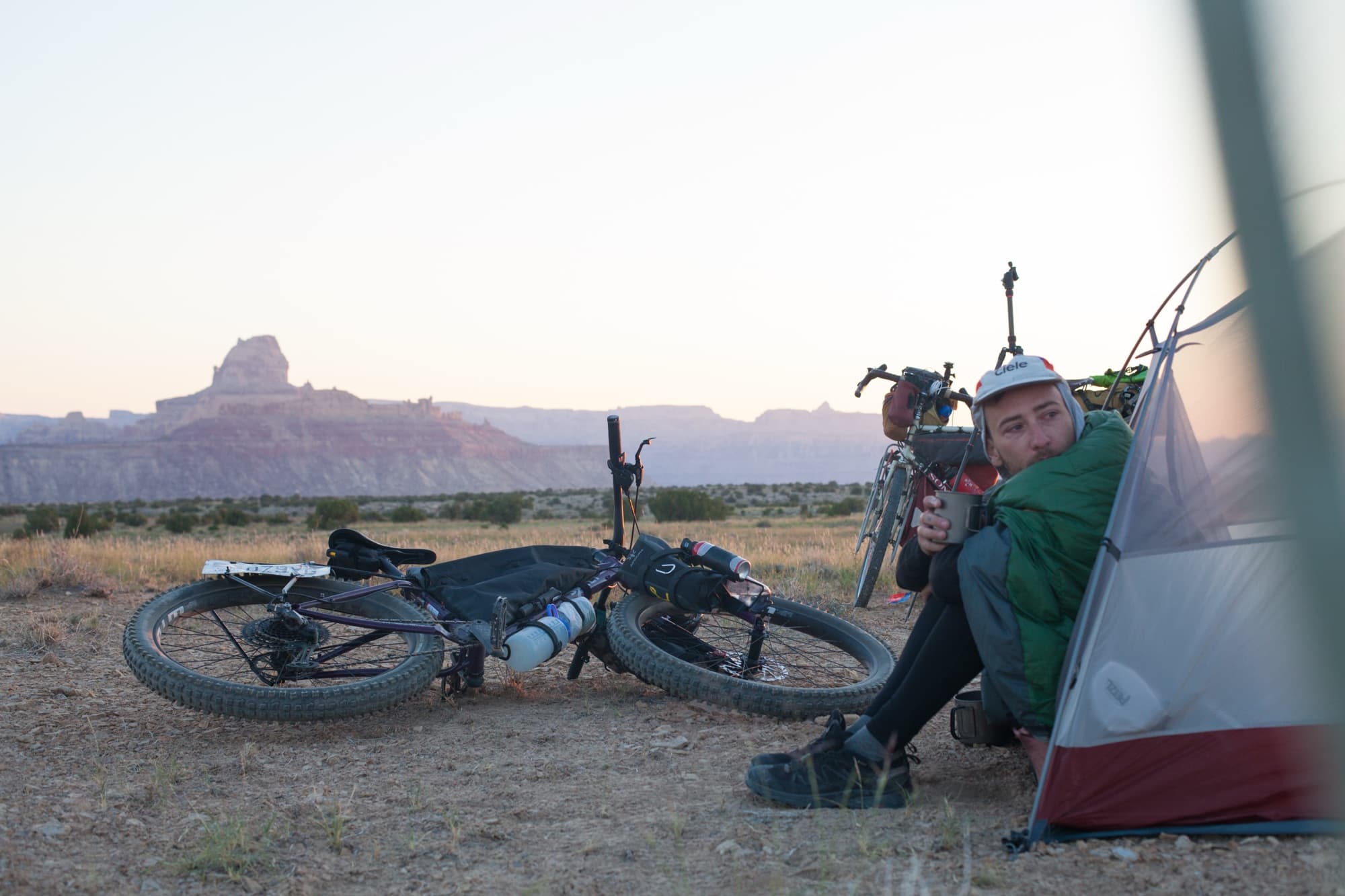 Crouched beside the tent at dusk, bikes laid down in the desert