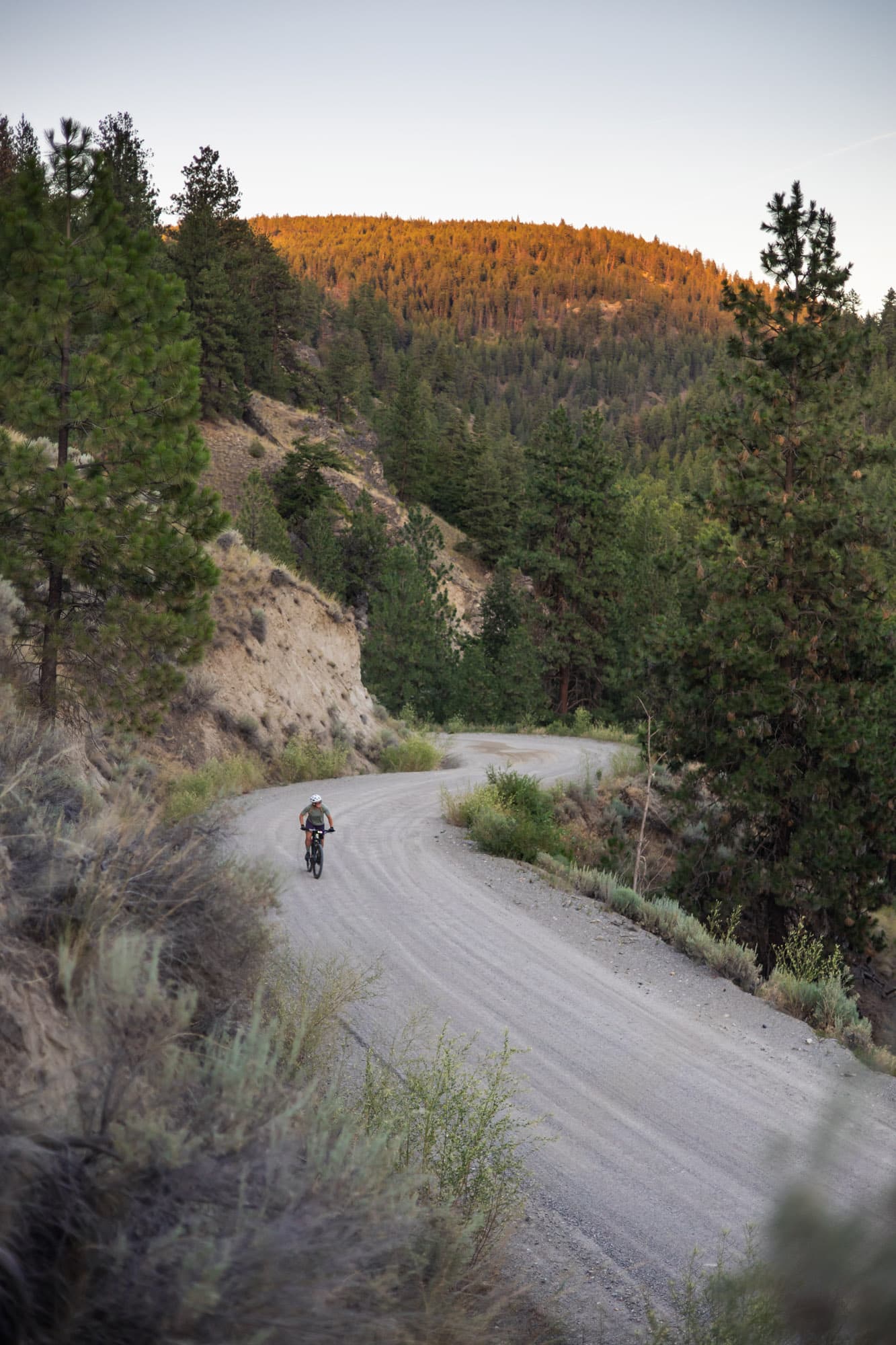 A rider descending a winding gravel road through dry hills.