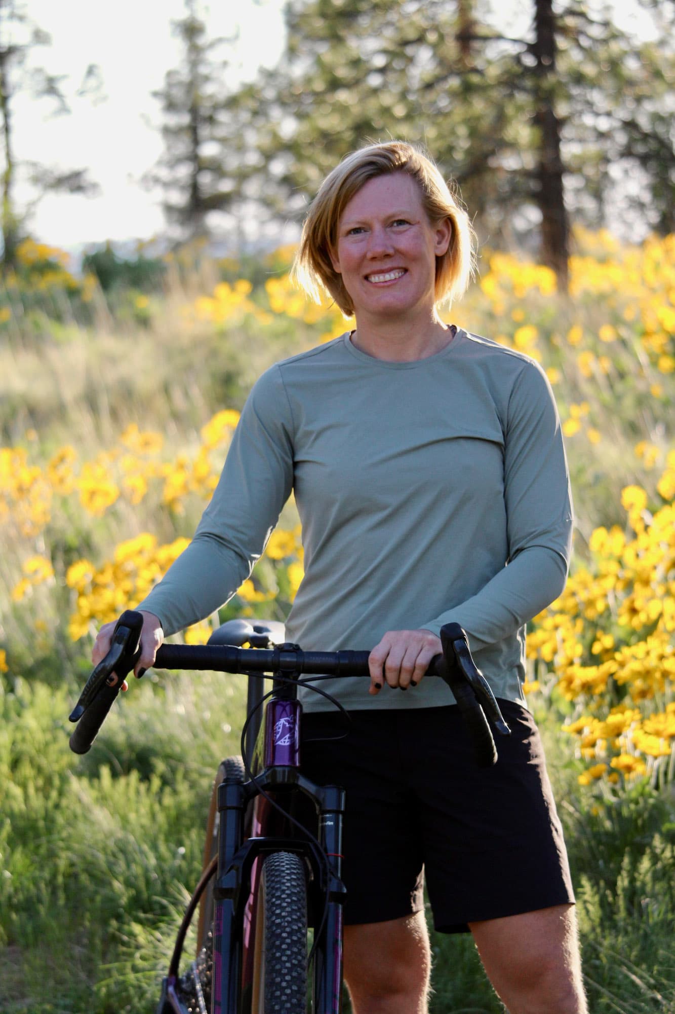 Meaghan with her bike among yellow wildflowers.