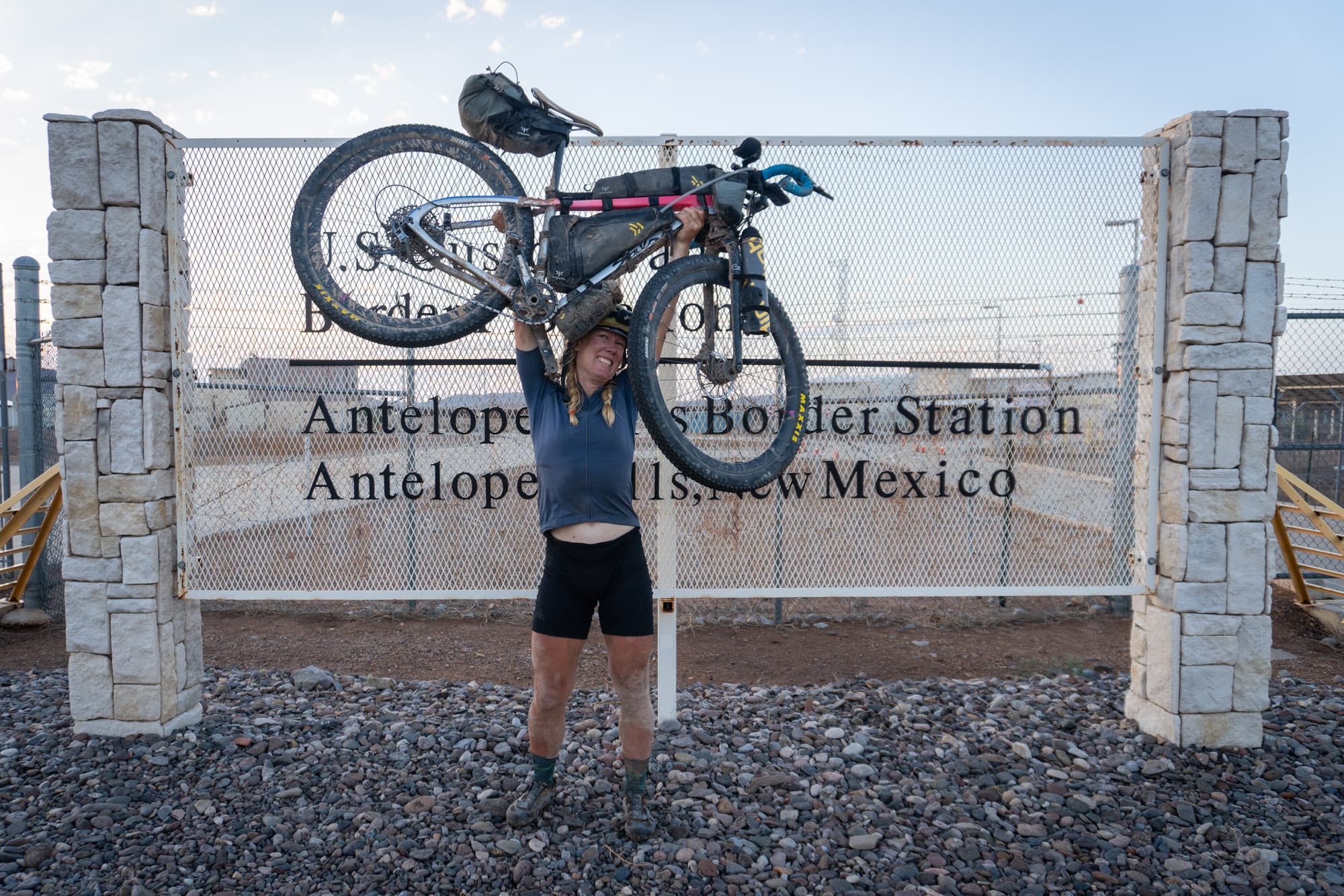 Meaghan hoists her bike overhead at the Antelope Wells border sign.