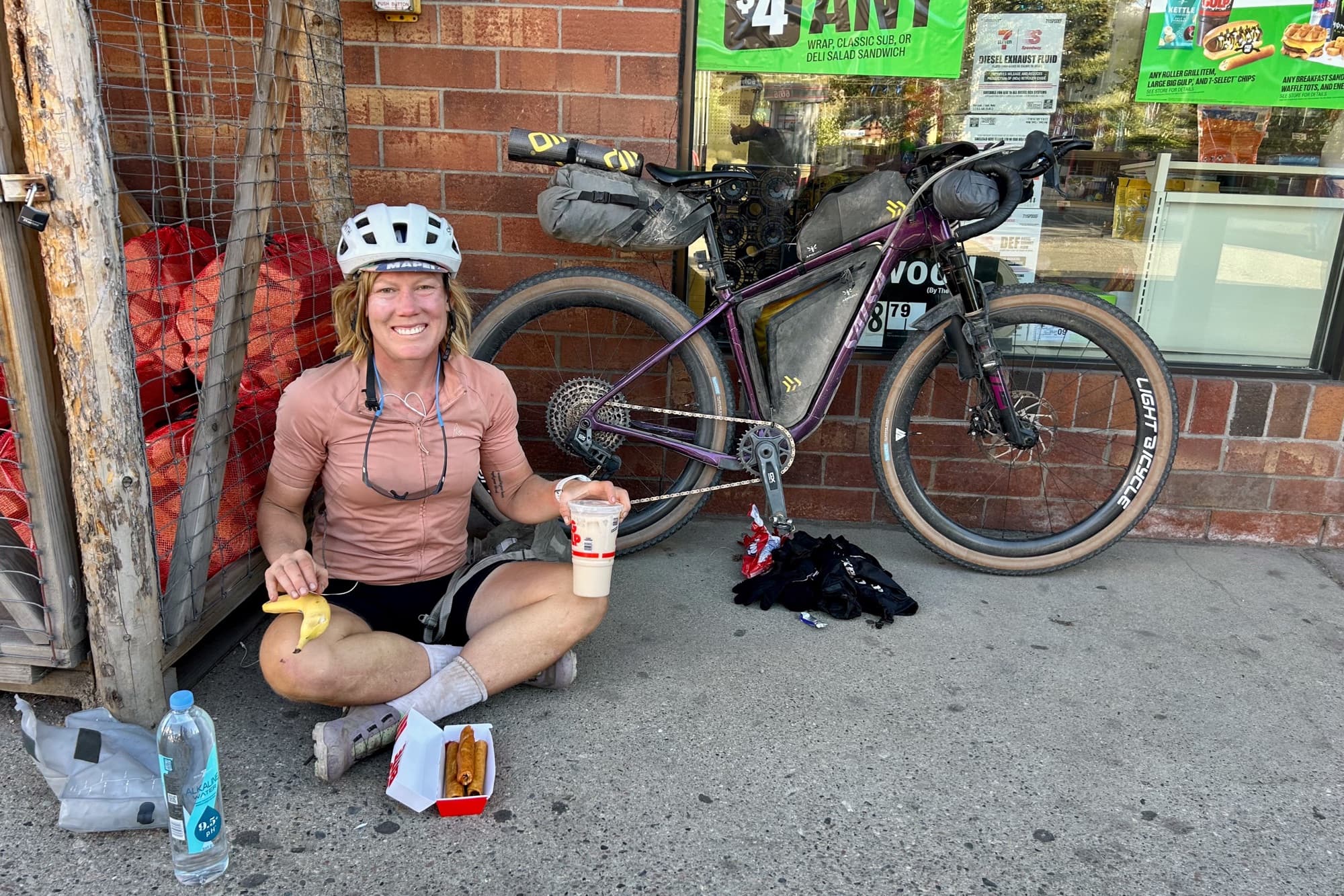 A sidewalk resupply meal outside a corner store, with Dolly parked against the wall