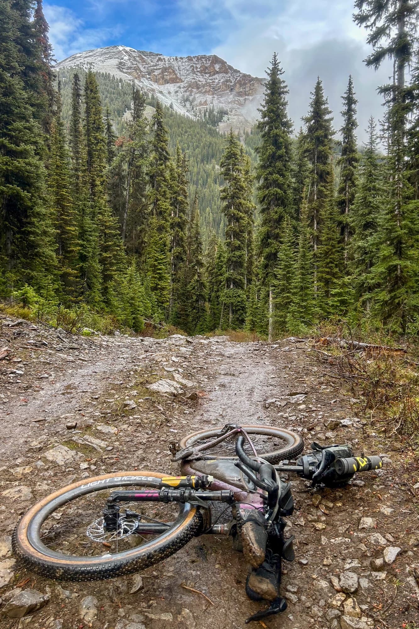 Meaghan's loaded bike rests on the rocky Koko Claims climb below a snowy peak